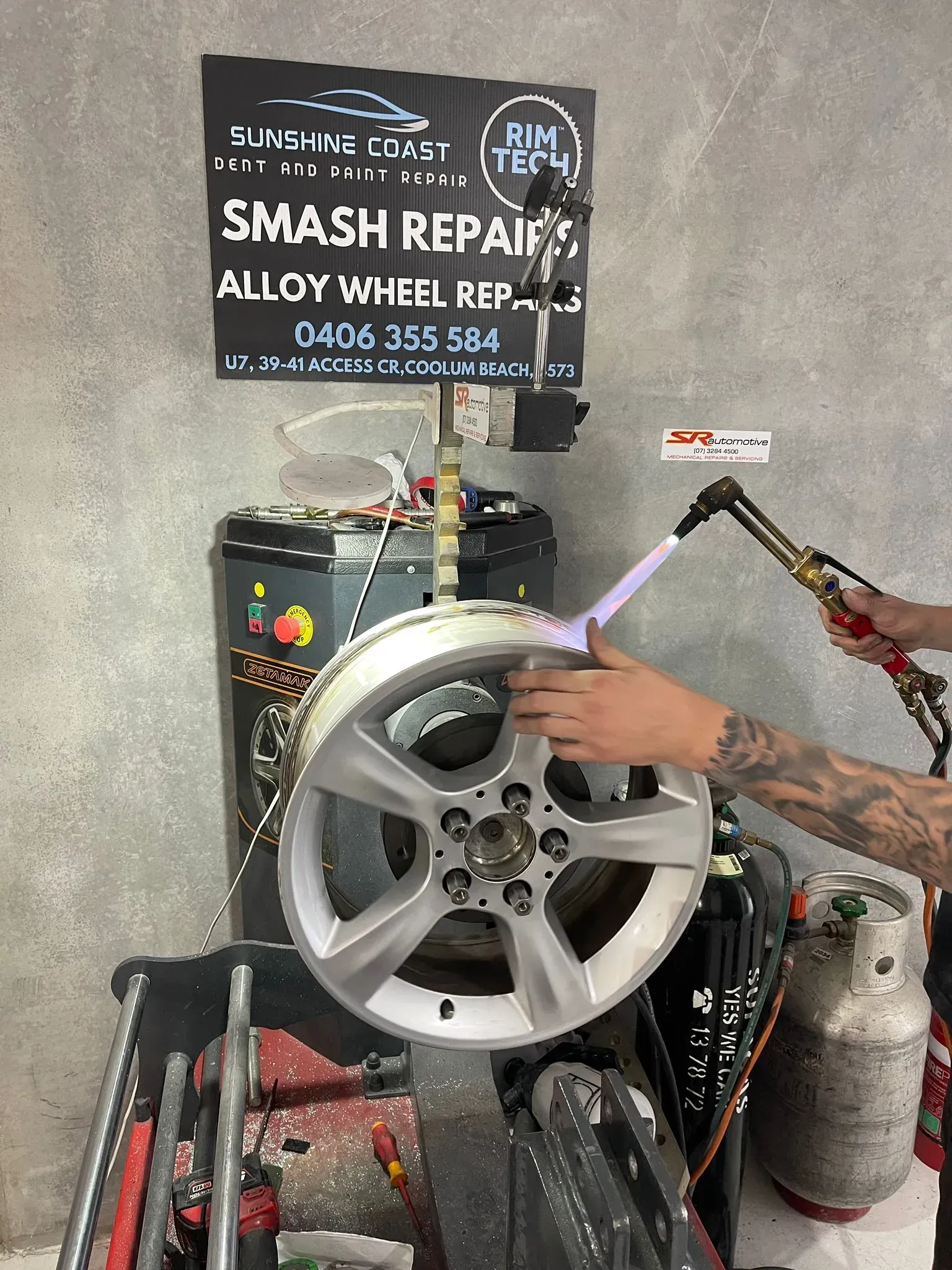 Person using a torch on a silver alloy wheel, a repair sign is above it. — Coolum Smash Repairs in Coolum Beach, QLD