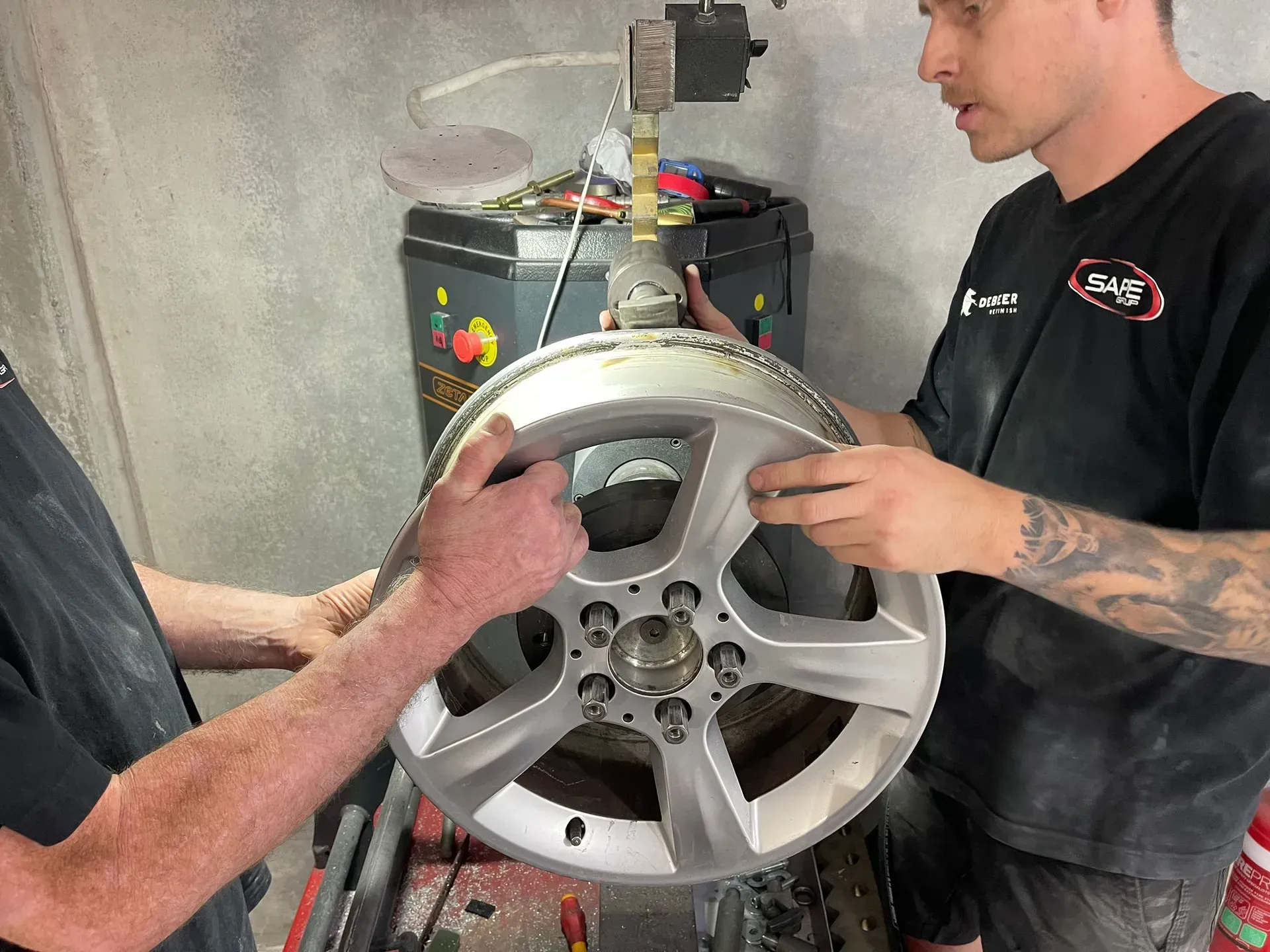Two people holding a silver car wheel in a workshop, near machinery. — Coolum Smash Repairs in Coolum Beach, QLD