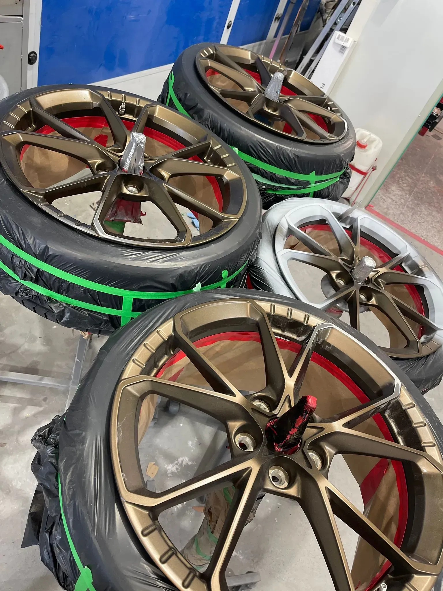Four gold-colored car wheels with red accents, and tires with green bands, in an indoor setting. — Coolum Smash Repairs in Coolum Beach, QLD