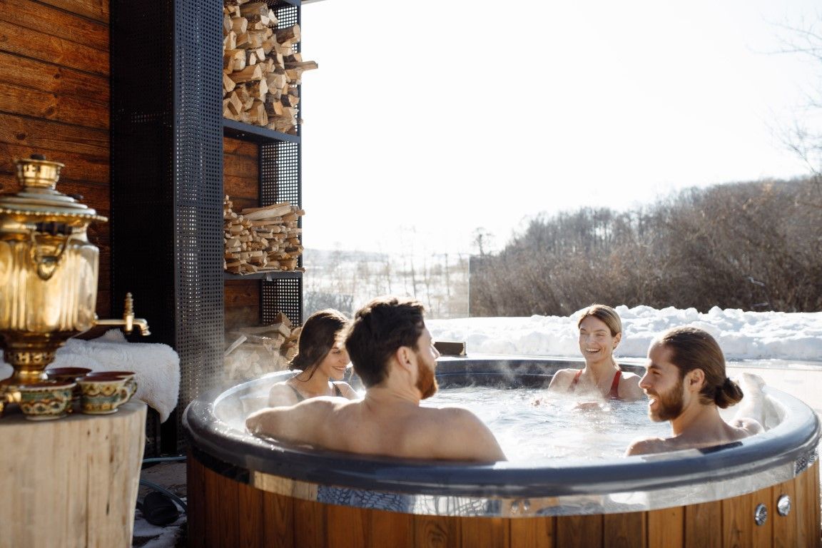 People relaxing in an outdoor hot tub beside a rustic cabin in a snowy landscape