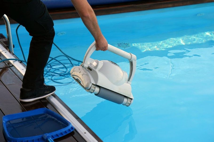 Person lowering a robotic pool cleaner into a blue swimming pool