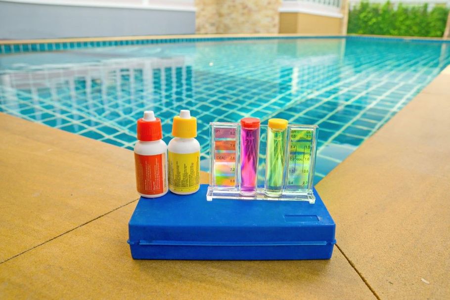 Poolside sunscreen bottles and colorful test tubes on a blue tray by a swimming pool