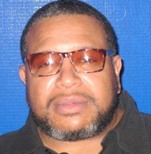 A man with glasses and a beard is standing in front of a blue wall