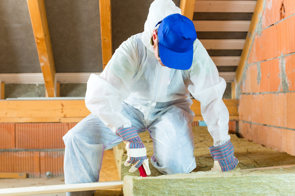 A man in a protective suit is kneeling down in an attic.