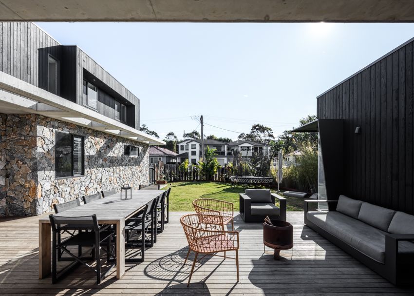 Modern outdoor patio with dining table, chairs, sofa, and a stone and black-paneled house — Make The Mark Building Services in Illawarra, NSW