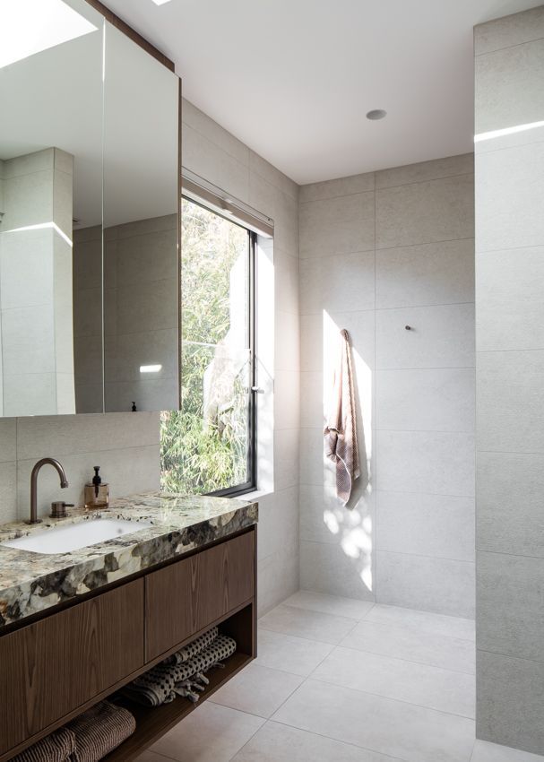 Modern bathroom with a wood vanity, stone countertop, large mirror, and natural light from a window — Make The Mark Building Services in Illawarra, NSW