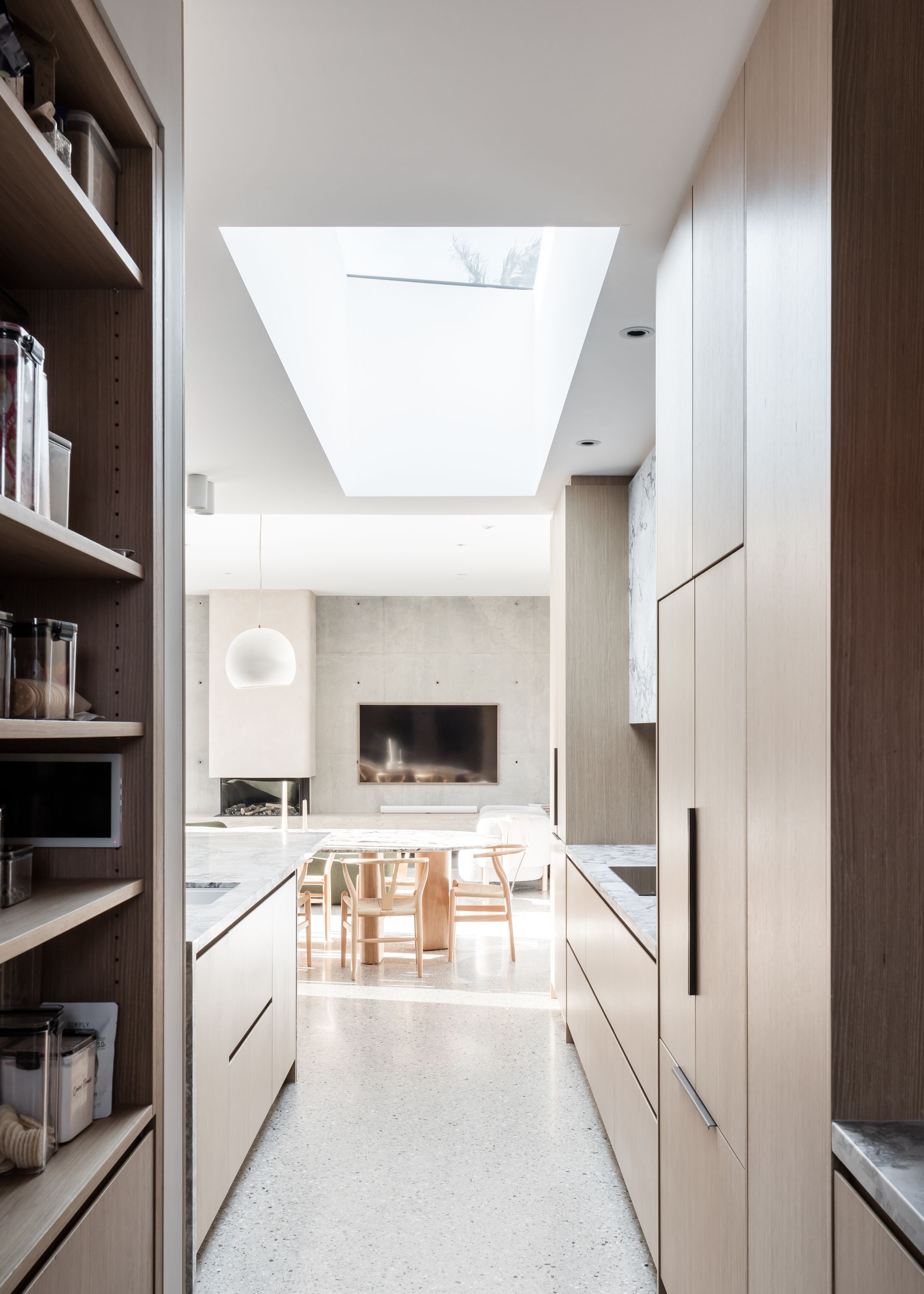 Long, narrow kitchen with skylight, light wood cabinets, terrazzo floor, and dining area at the end — Make The Mark Building Services in Mangerton, NSW