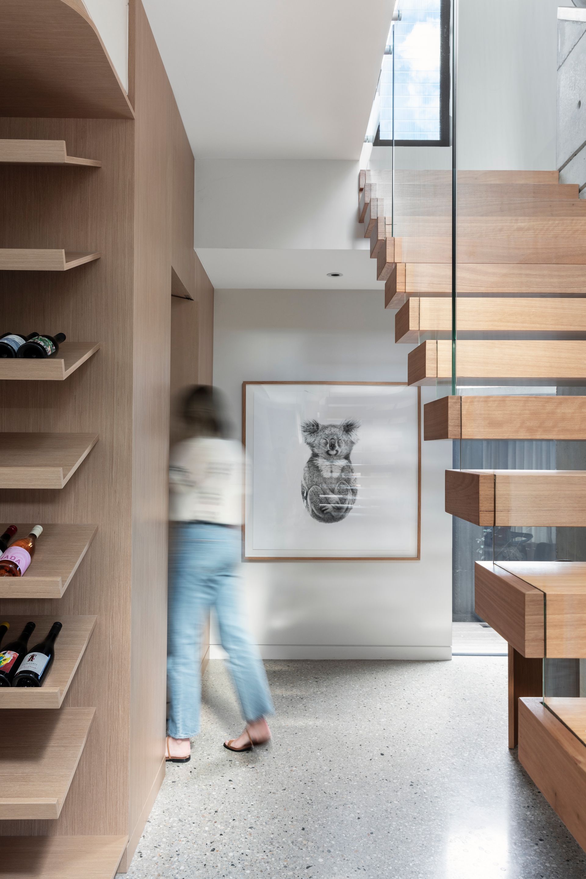 Hallway with wooden stairs, built-in wine rack, large framed artwork, and person walking — Make The Mark Building Services in Illawarra, NSW