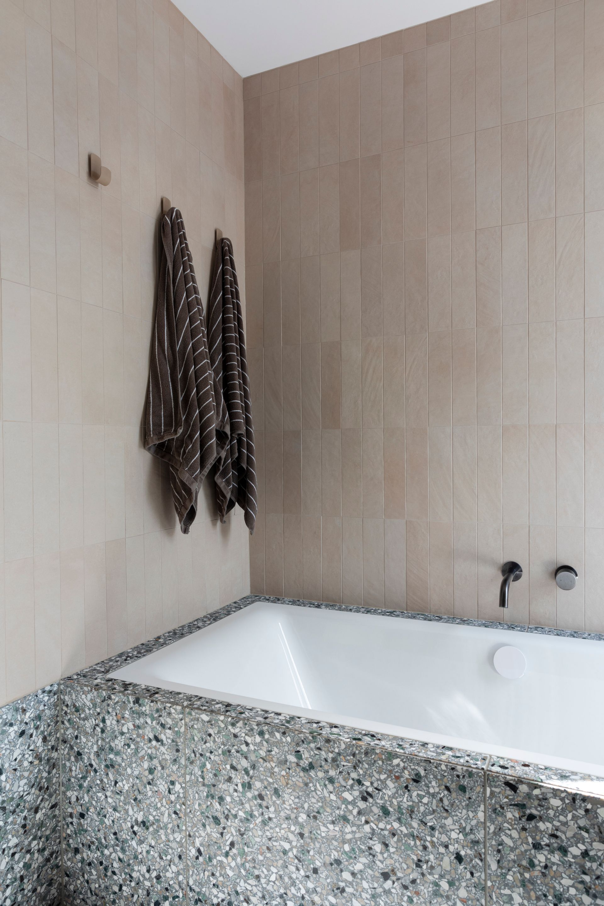 Bathroom with a white bathtub and textured stone surround. Beige tile walls with towels hanging — Make The Mark Building Services in Illawarra, NSW
