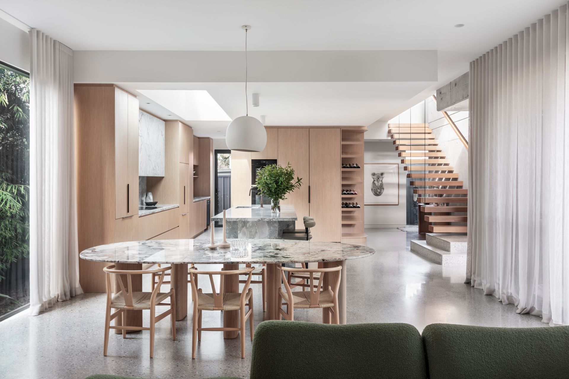 Modern kitchen and dining area with marble table, wooden cabinets, and a staircase — Make The Mark Building Services in Illawarra, NSW