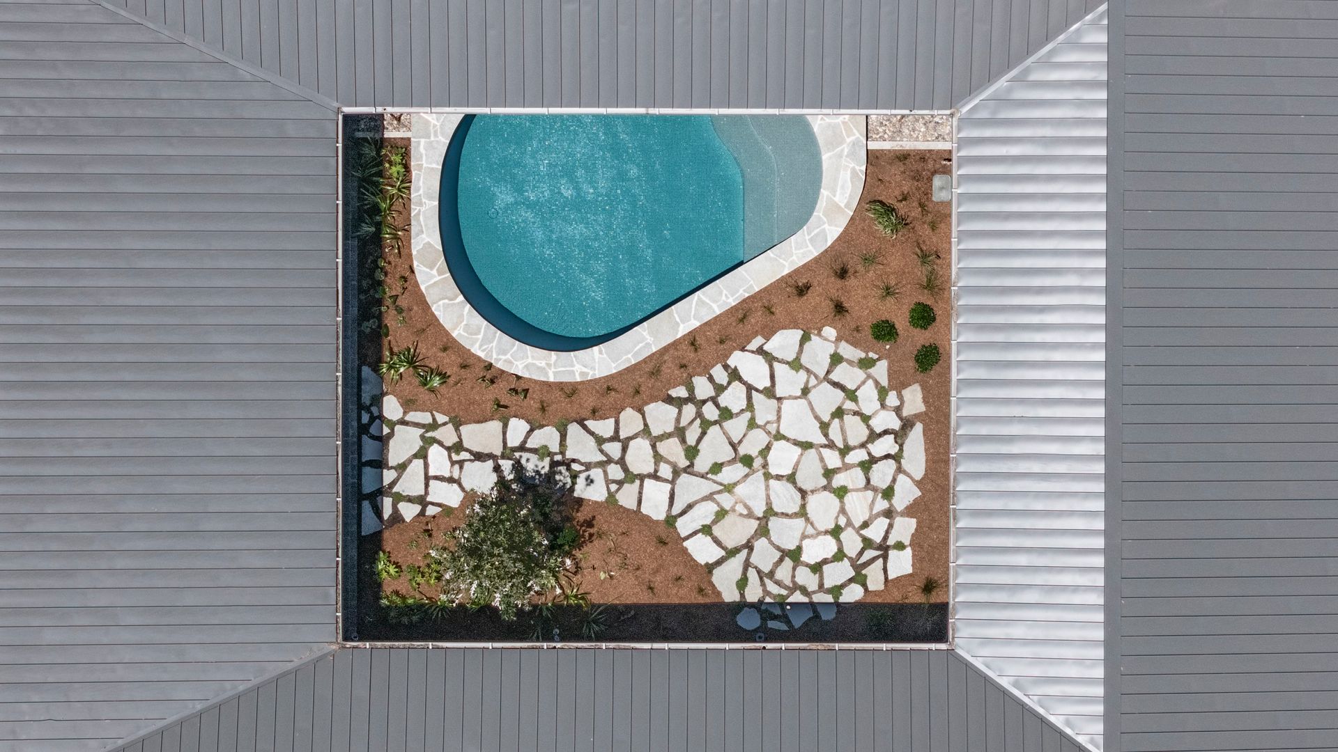 Overhead view of a courtyard with a kidney-shaped pool, stone pathway, and surrounding light gray roof — Make The Mark Building Services in Illawarra, NSW