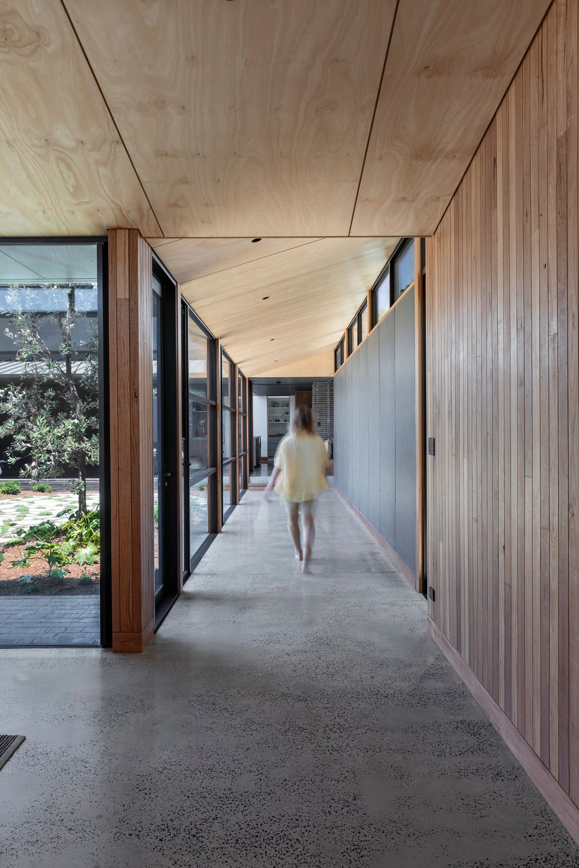 Person walking down a long, modern hallway with floor-to-ceiling windows and wooden paneling — Make The Mark Building Services in Mangerton, NSW