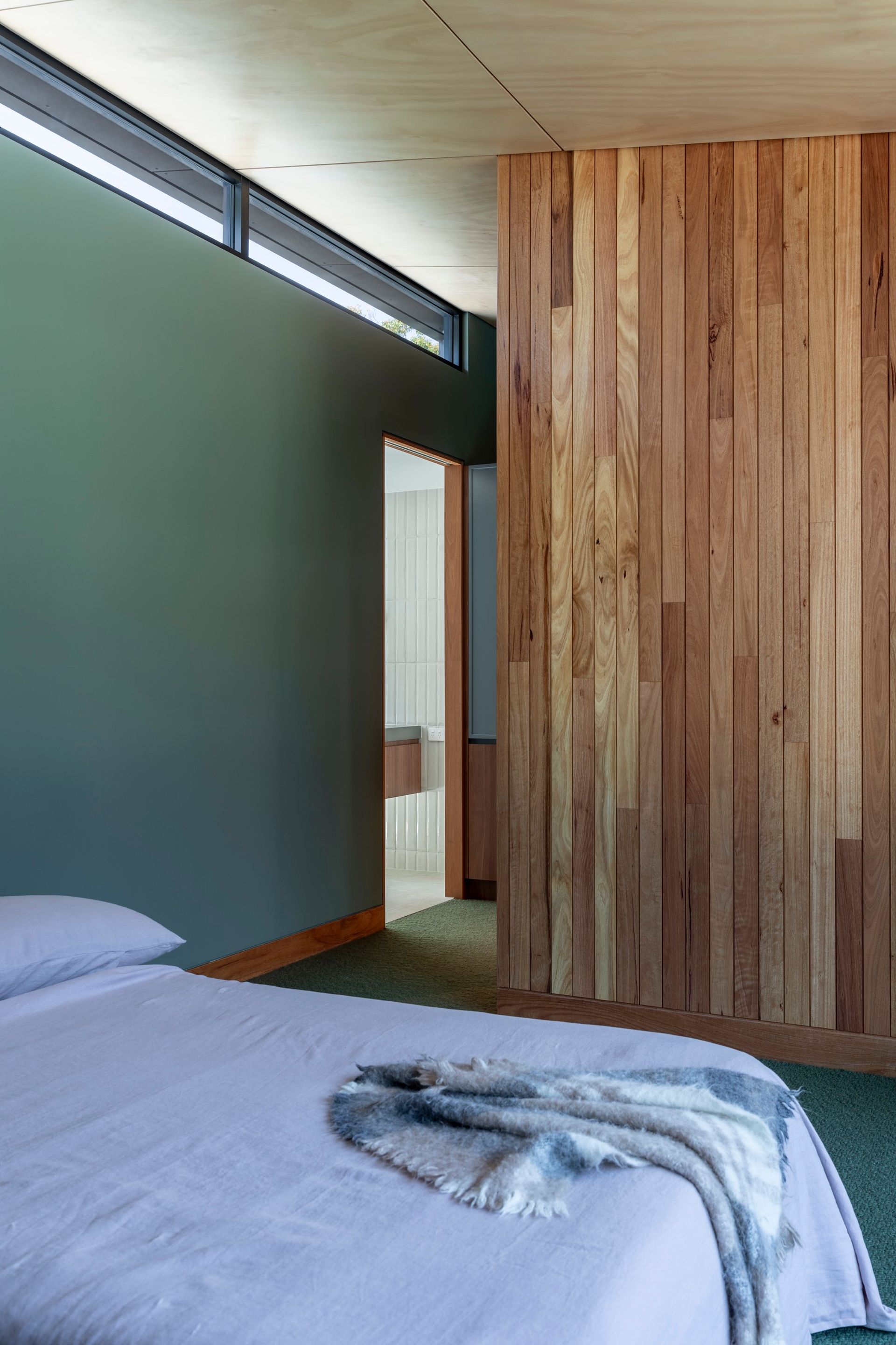 Bedroom with wood panel wall, green wall, light-colored bed, and a glimpse of a bathroom — Make The Mark Building Services in Illawarra, NSW