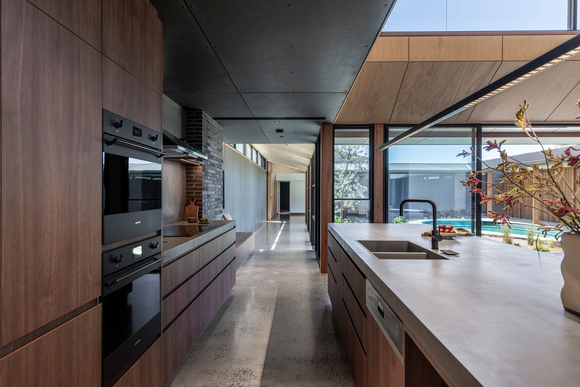 Modern kitchen with dark wood cabinets, concrete countertops, and a view of a pool — Make The Mark Building Services in Illawarra, NSW