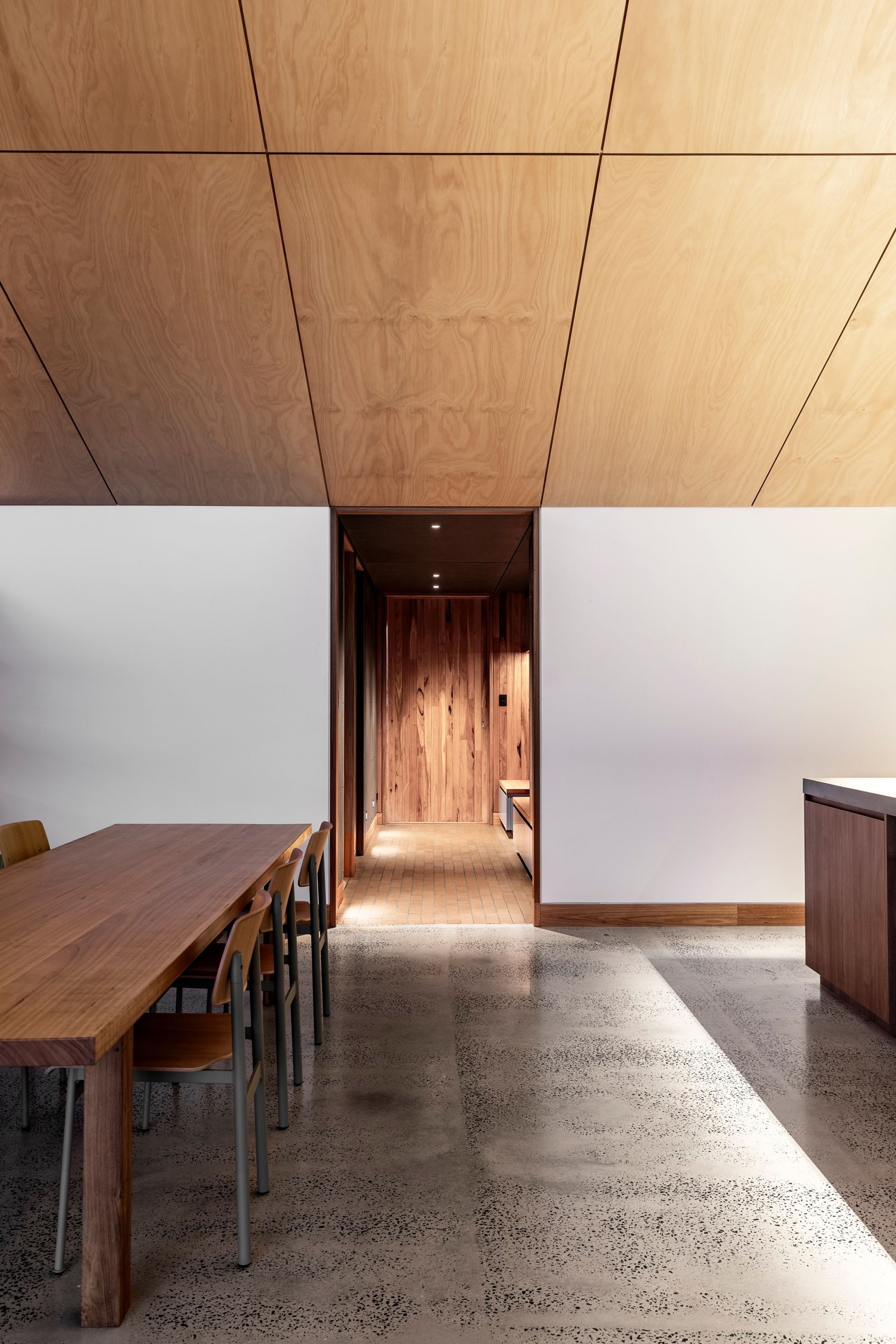 Wooden dining area with long table, concrete floor, and wood panel ceiling; leads to a hallway — Make The Mark Building Services in Illawarra, NSW