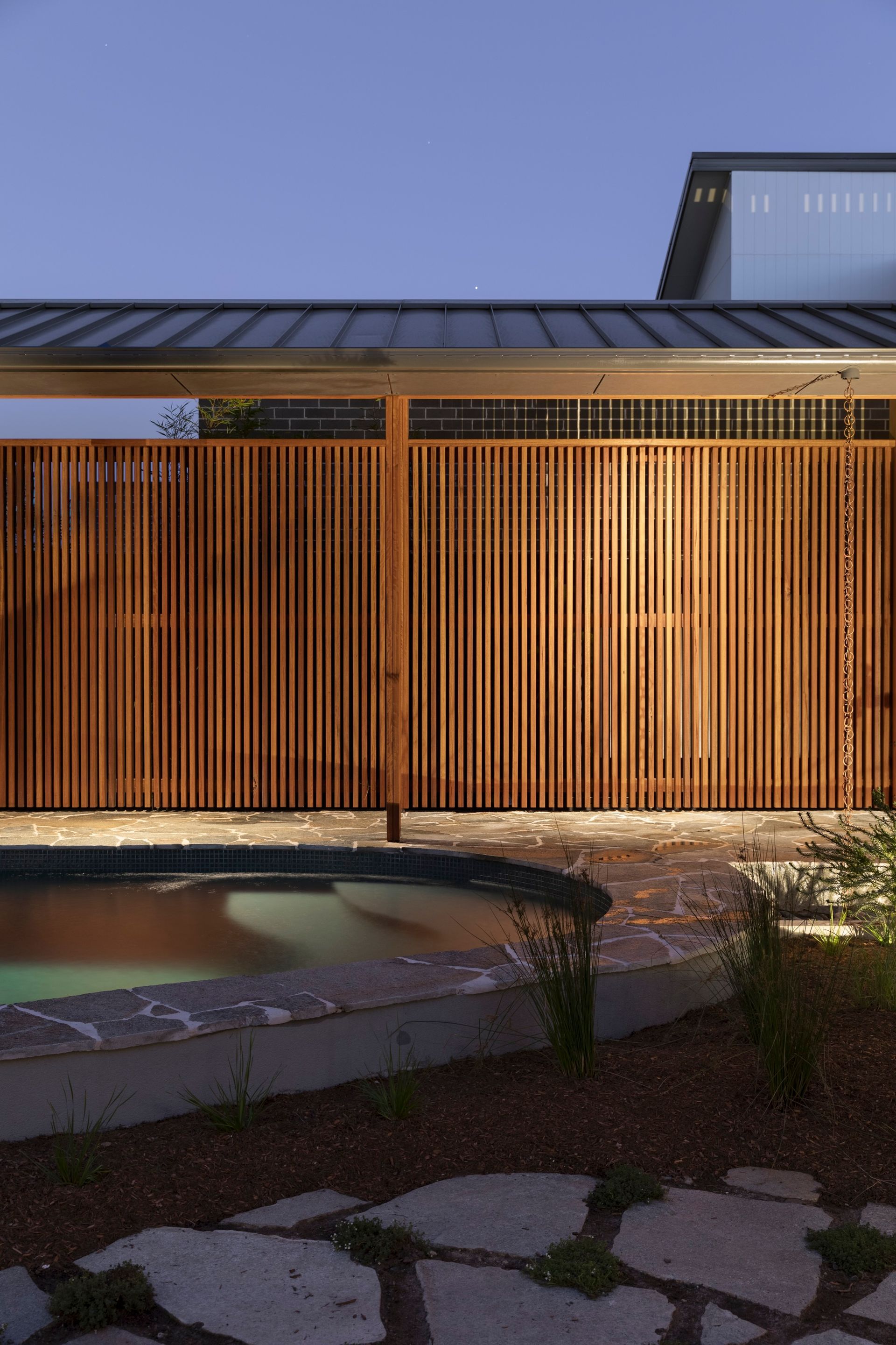 Wooden fence with vertical slats lit from below, bordering a pool and stone patio at dusk — Make The Mark Building Services in Illawarra, NSW