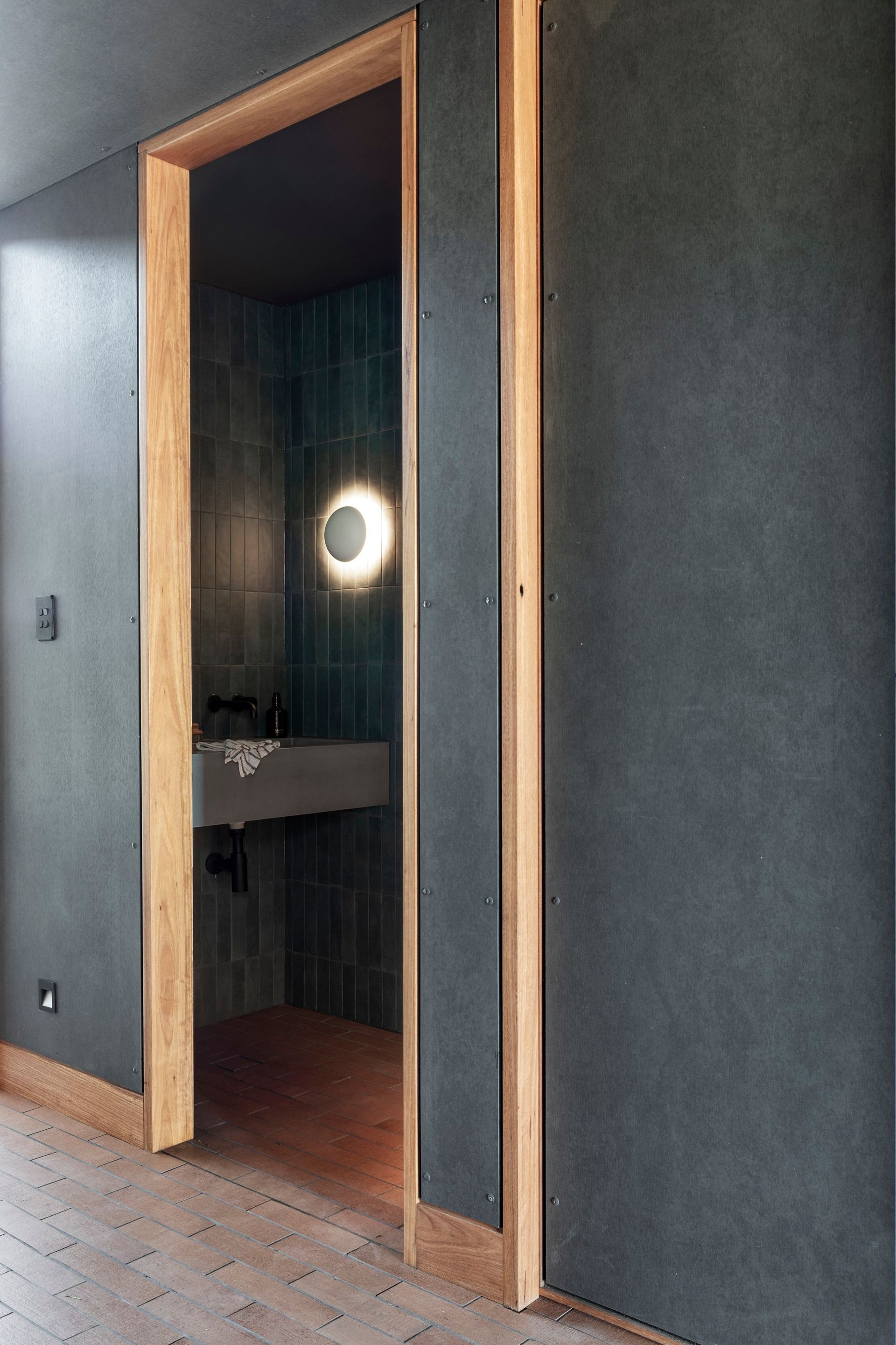 Doorway to a bathroom with green tile walls and a round light fixture — Make The Mark Building Services in Illawarra, NSW