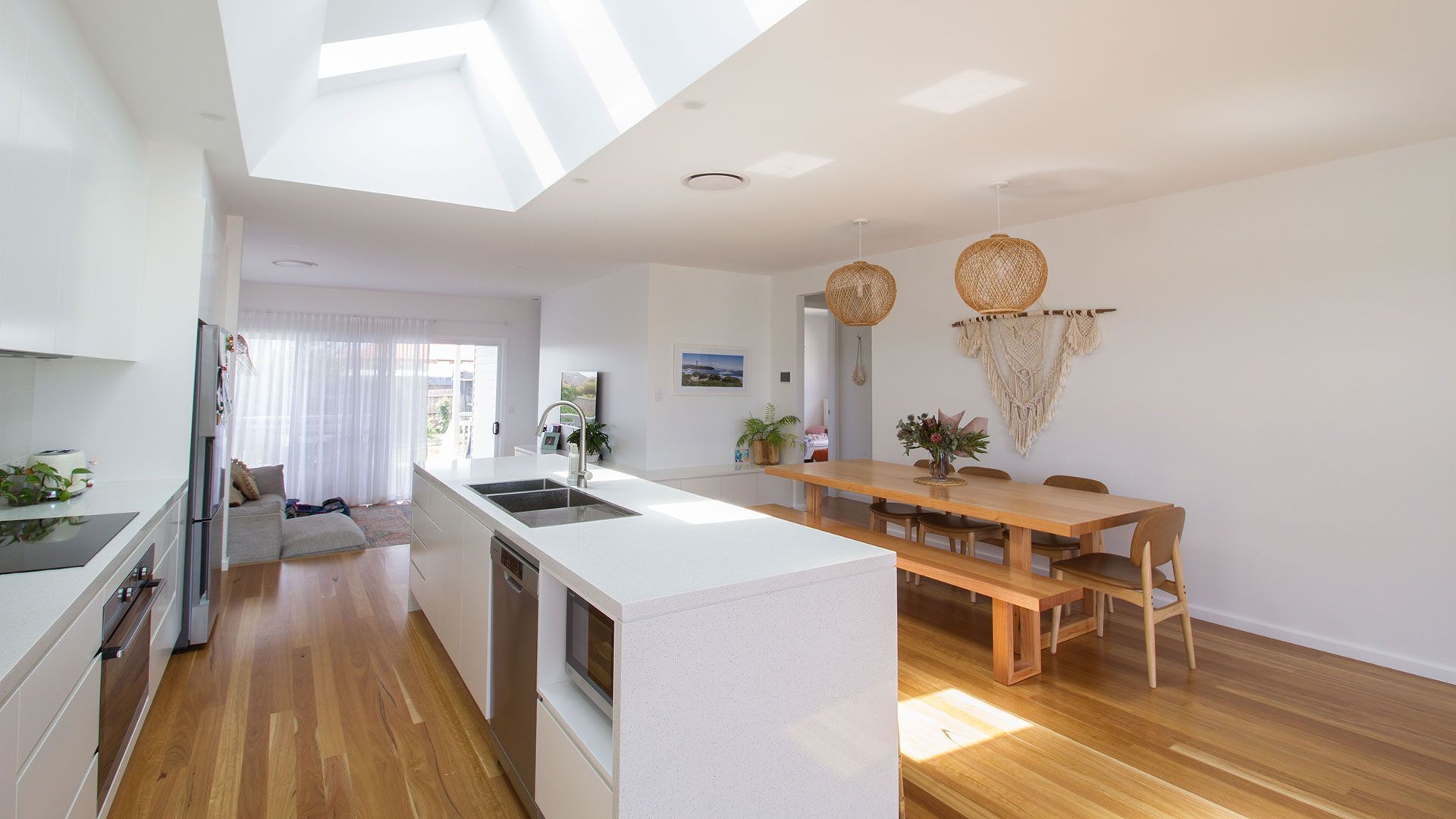 Bright, modern open-plan kitchen and dining area with skylights, white cabinets, wooden floor and table — Make The Mark Building Services in Mangerton, NSW