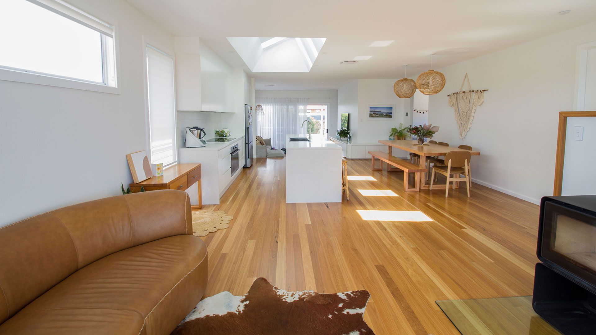 Bright, modern living space with wooden floors, white walls, and a large skylight. Features a leather sofa, dining area, and a kitchen island — Make The Mark Building Services in Mangerton, NSW