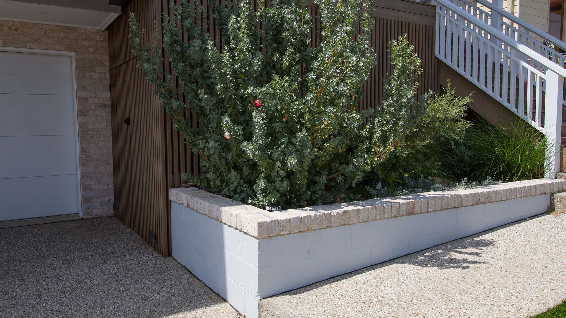 Concrete planter with green plants, next to a garage and stairs, on a pebble surface — Make The Mark Building Services in Mangerton, NSW
