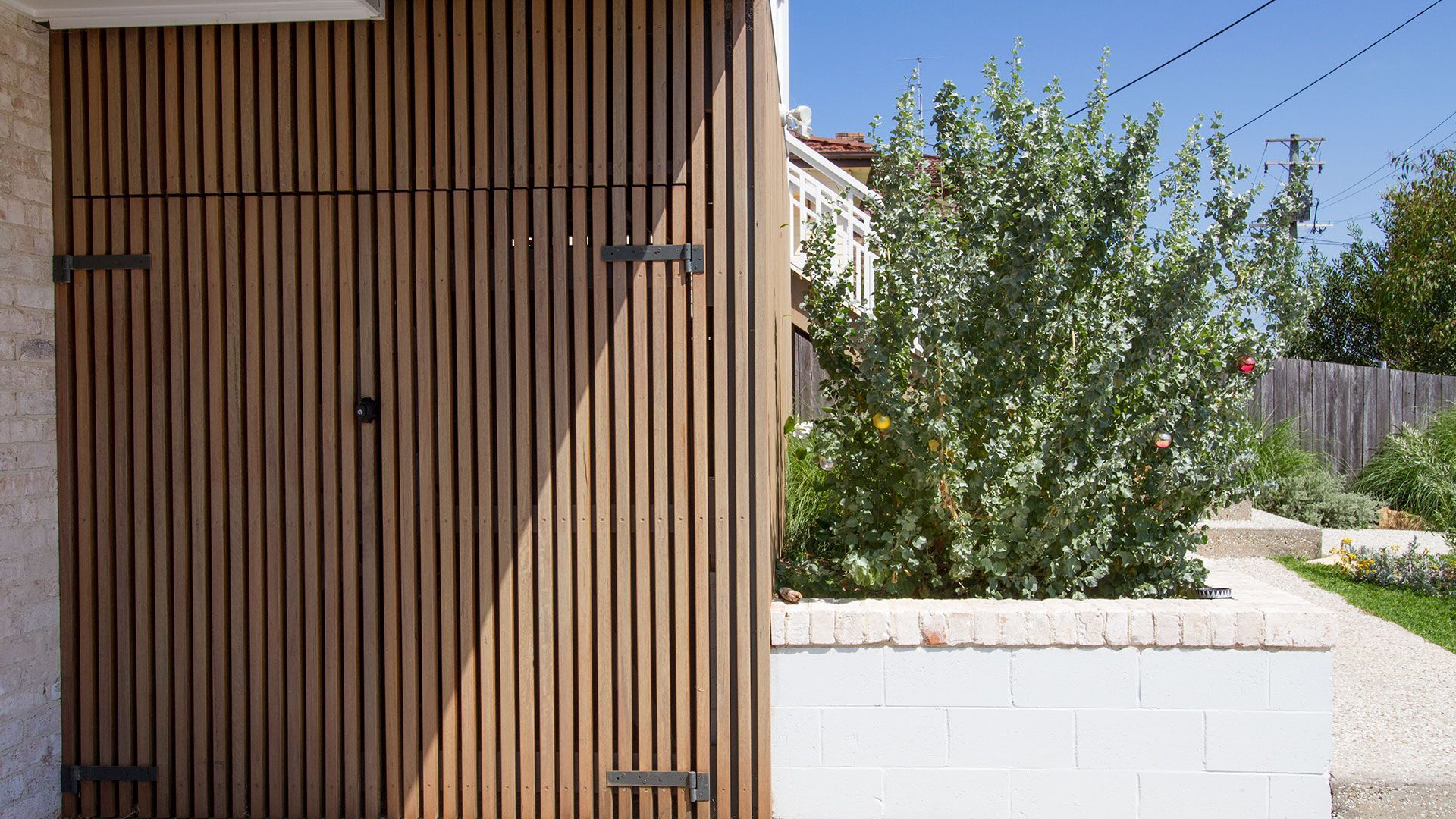 Wooden slat door with black hinges, next to white wall and garden with greenery — Make The Mark Building Services in Mangerton, NSW