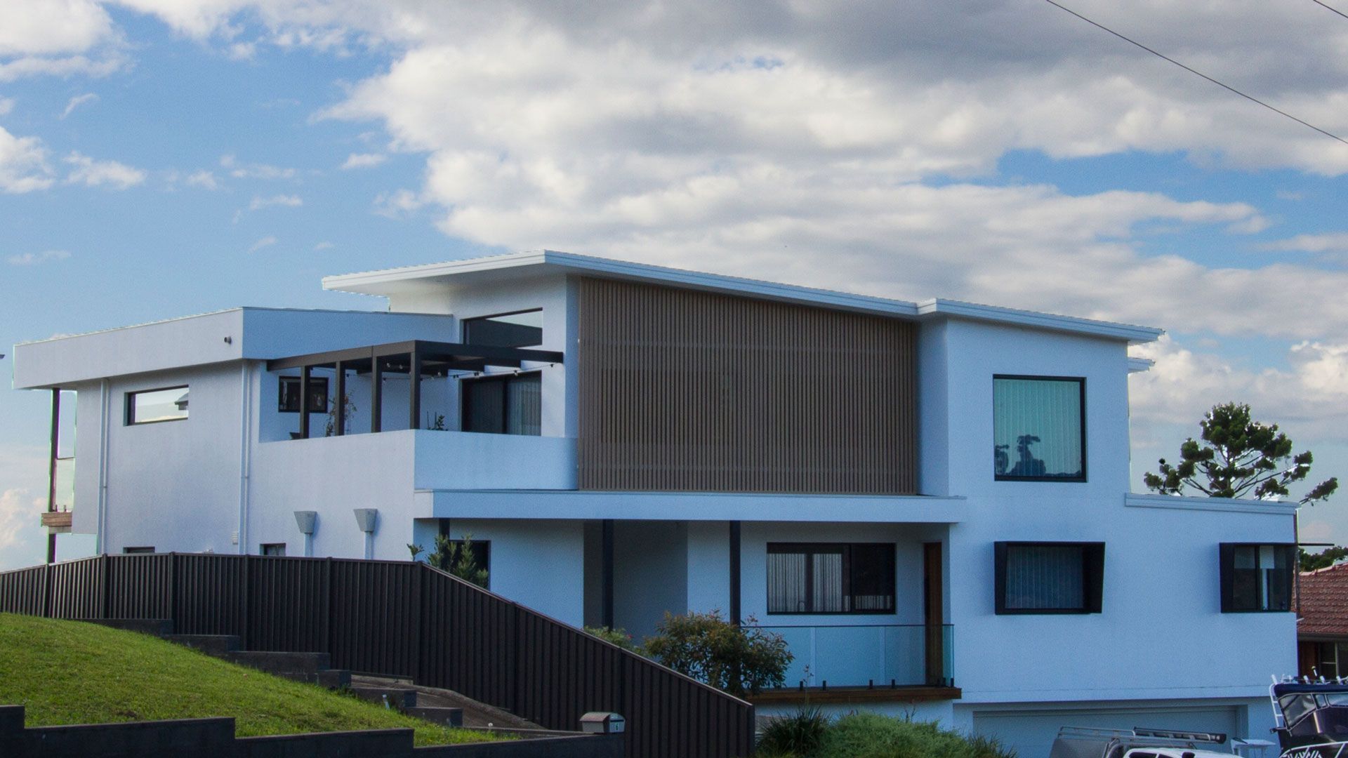Modern white house with wood paneling, multiple windows, and a balcony against a cloudy sky  — Make The Mark Building Services in Illawarra, NSW