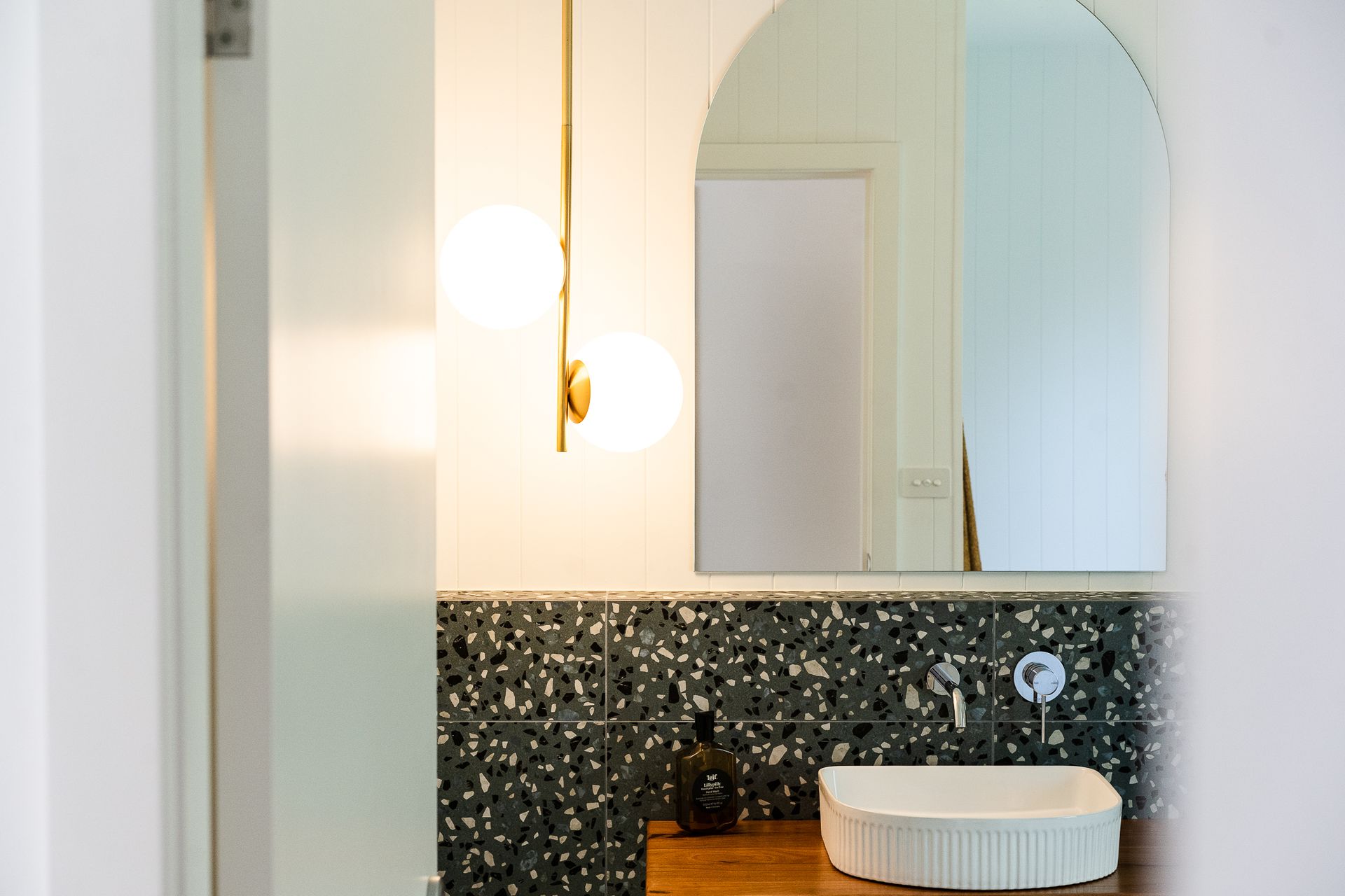 Bathroom interior with a white sink, patterned backsplash, and an arched mirror. A gold light fixture hangs from the ceiling - Make The Mark Building Services in Mangerton, NSW