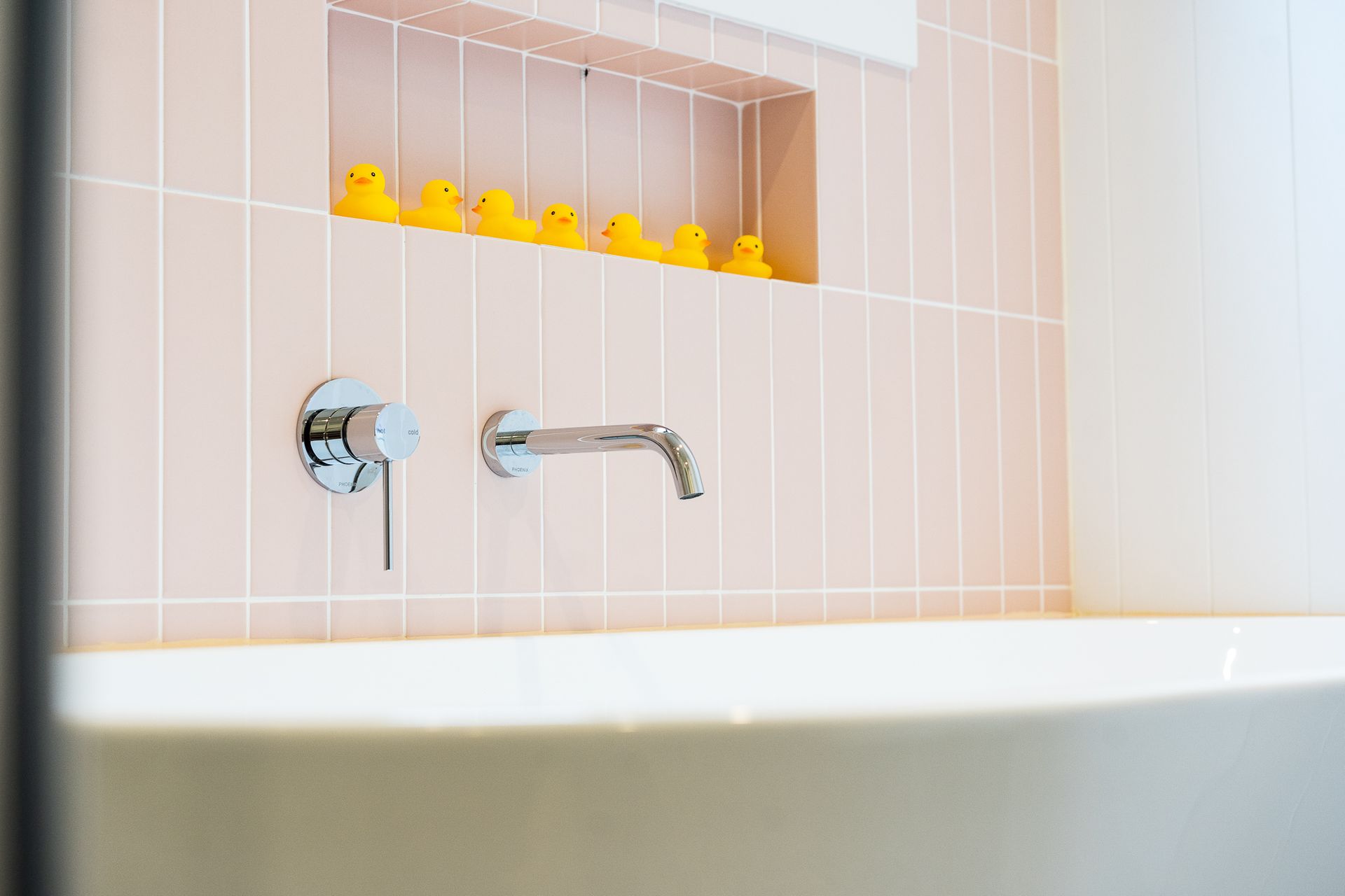 A white bathtub with chrome faucet. Pink tiled wall with a recessed shelf holding yellow rubber duckies - Make The Mark Building Services in Mangerton, NSW