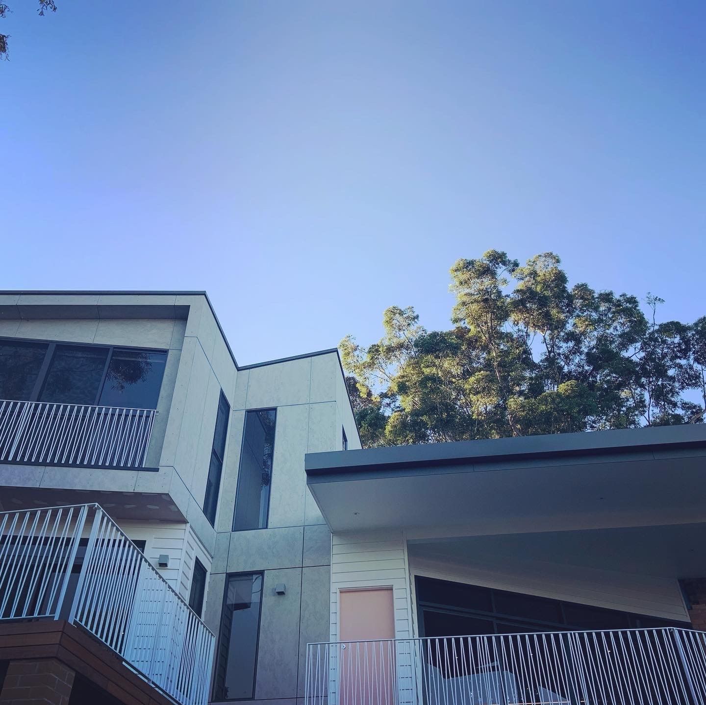 Modern white building with black windows and a metal railing against a clear blue sky - Make The Mark Building Services in Mangerton, NSW