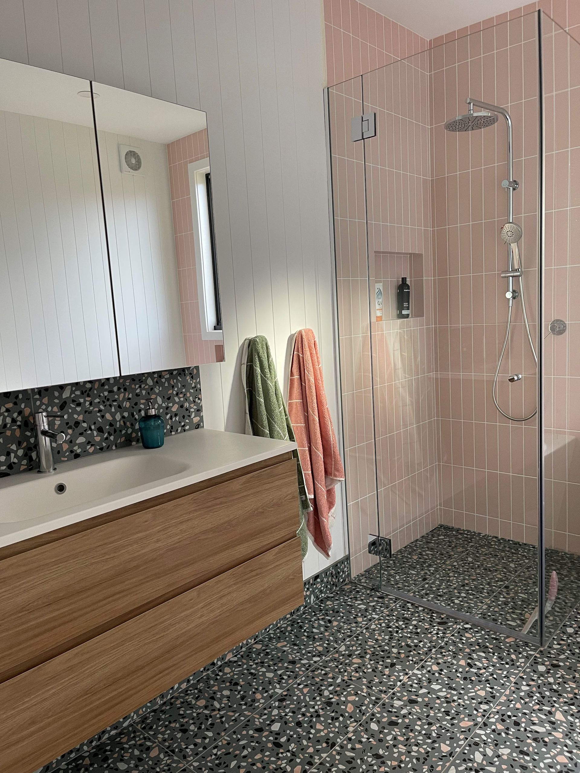 Modern bathroom with pink tiled shower, pebble floor, wooden vanity, and large mirror - Make The Mark Building Services in Mangerton, NSW
