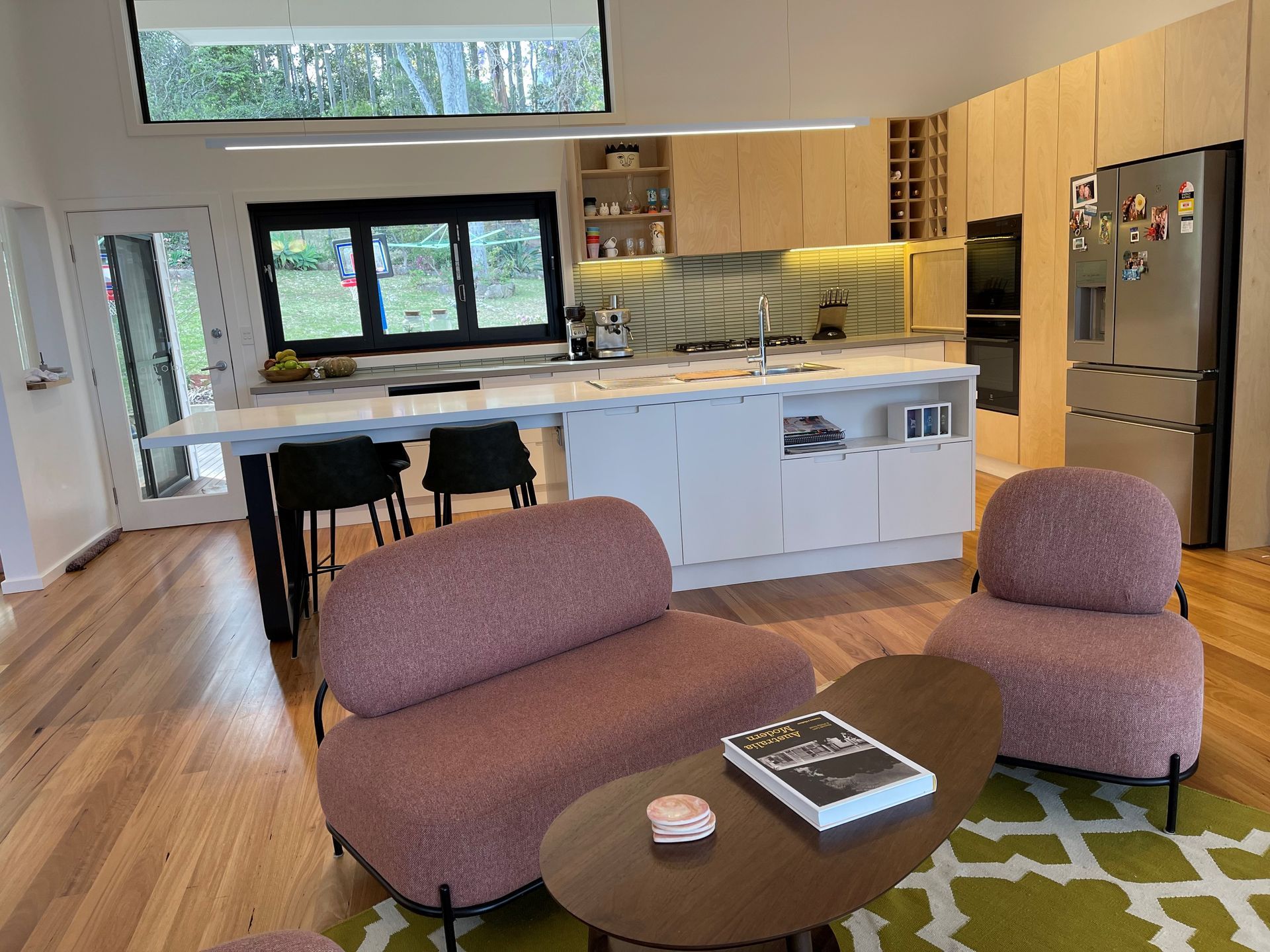 Modern kitchen with island, seating area with pink chairs, wooden floors - Make The Mark Building Services in Mangerton, NSW