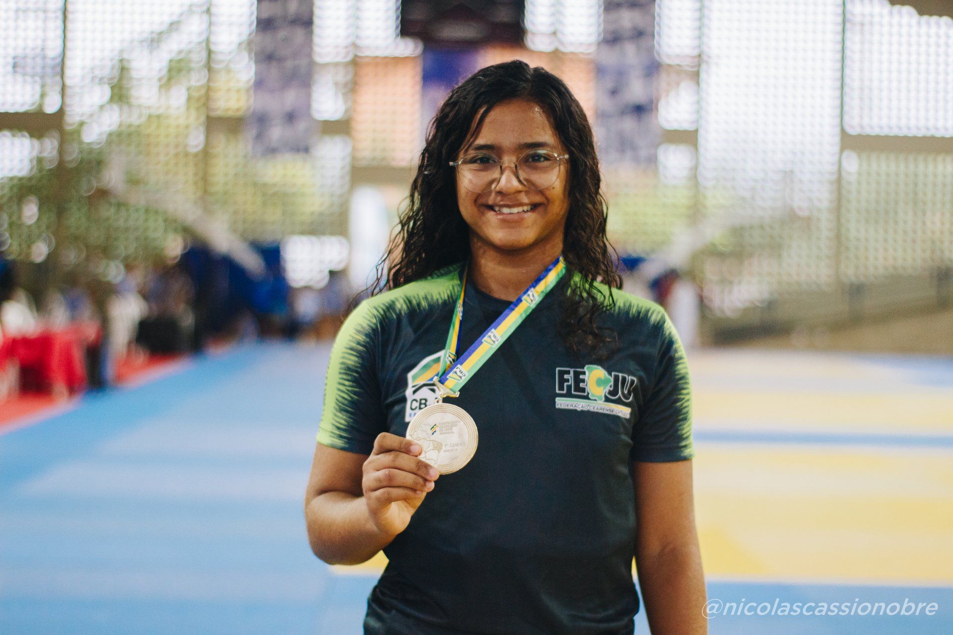 Flaiane Tomé em primeiro plano segurando uma medalha de ouro.