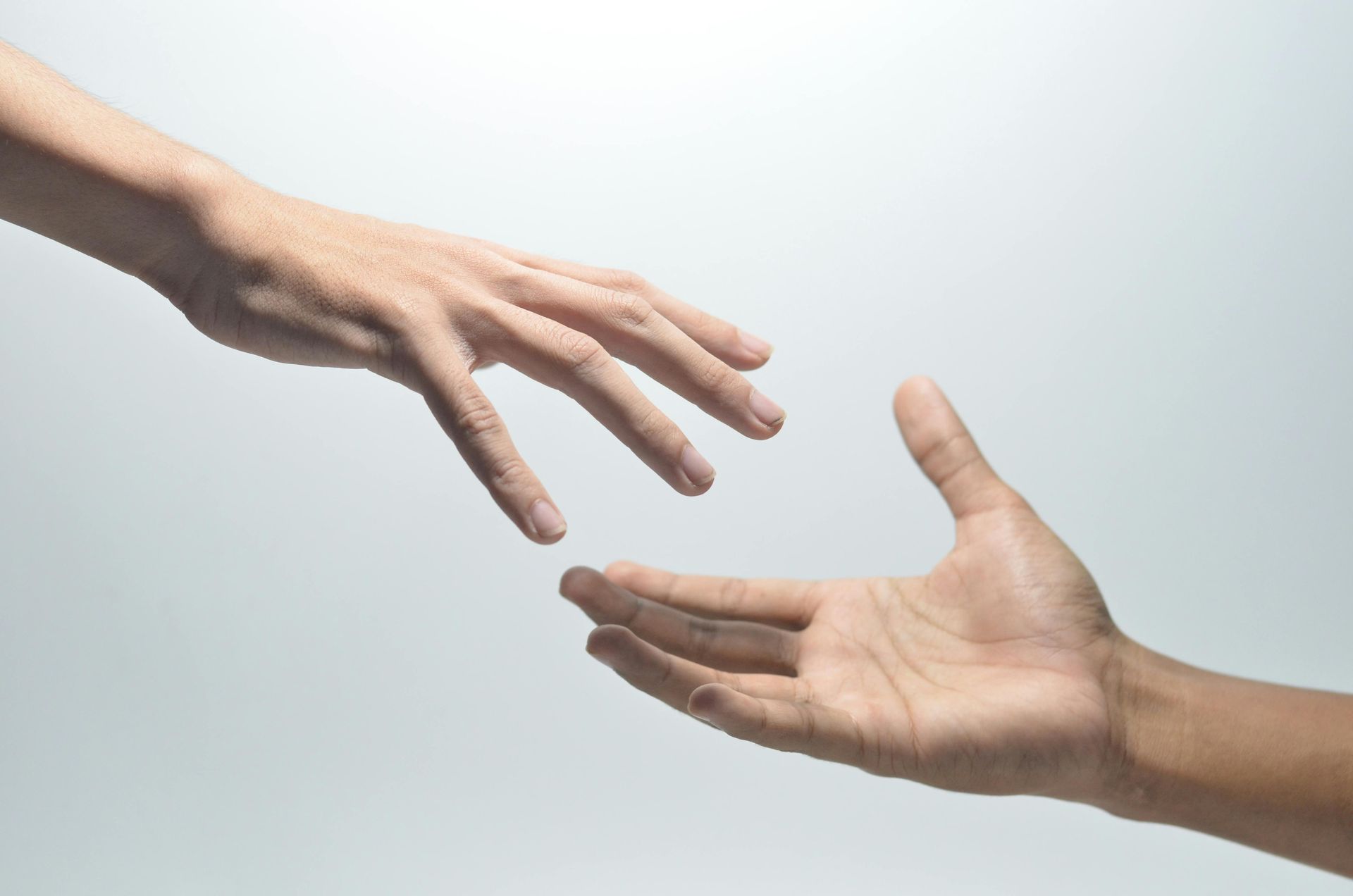 Two hands reaching toward each other, one light-skinned, the other darker, against a gray background.