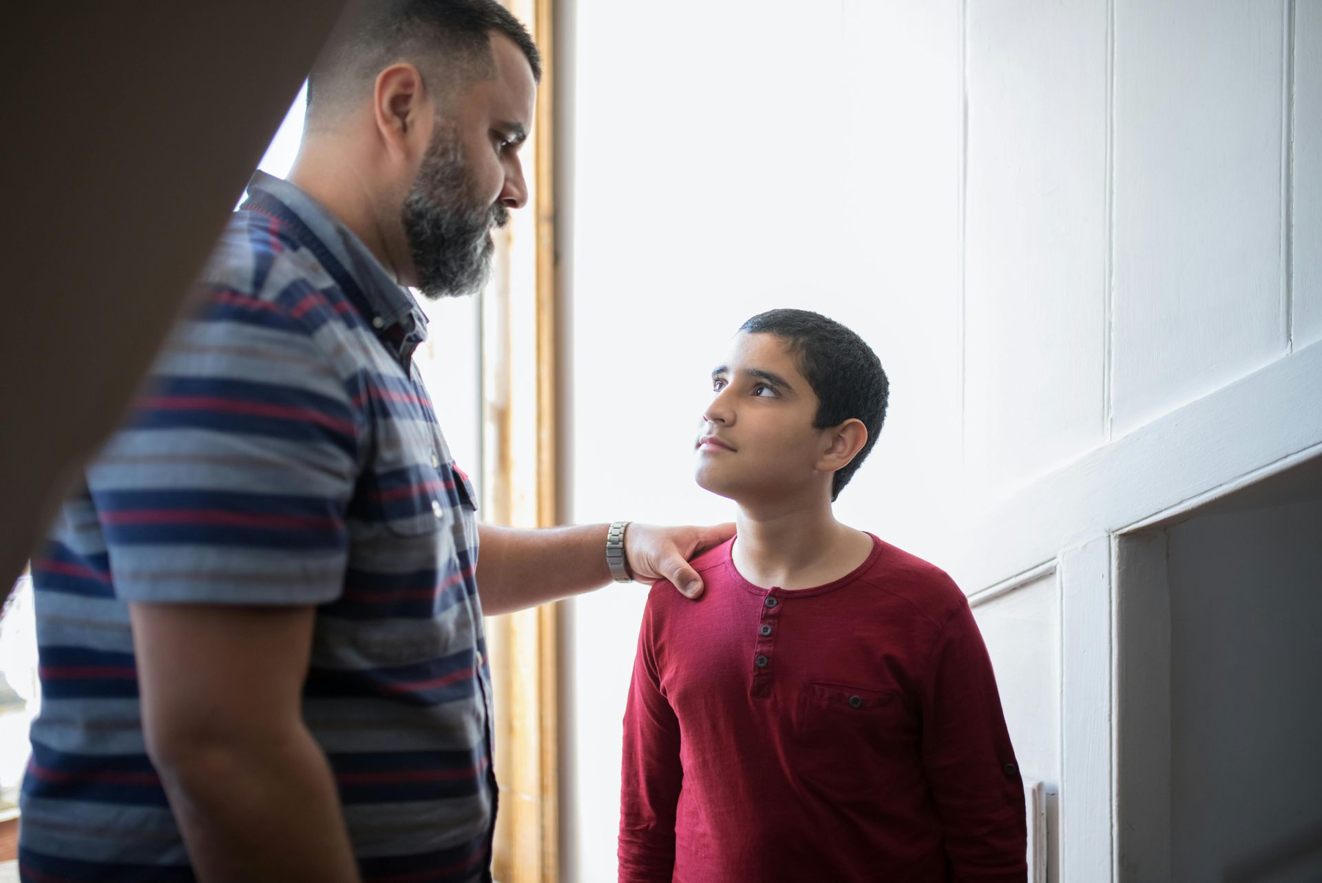 Man with beard places hand on boy's shoulder, looking at him; doorway setting.