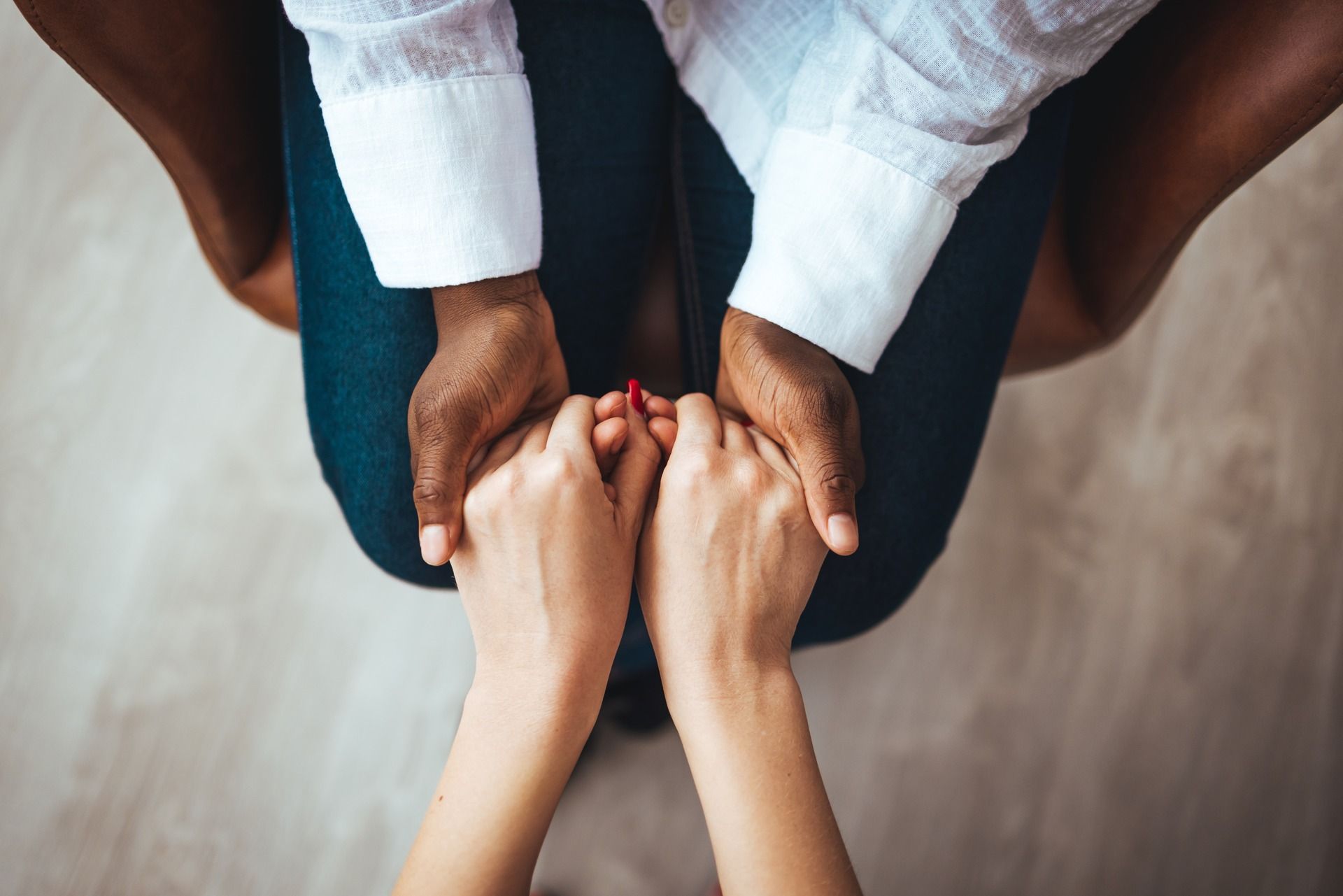 Two pairs of hands held together in a gesture of comfort, with one pair resting gently atop the other.