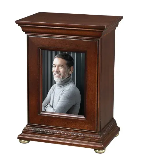 Wooden memorial urn with a framed portrait on the front and brass feet