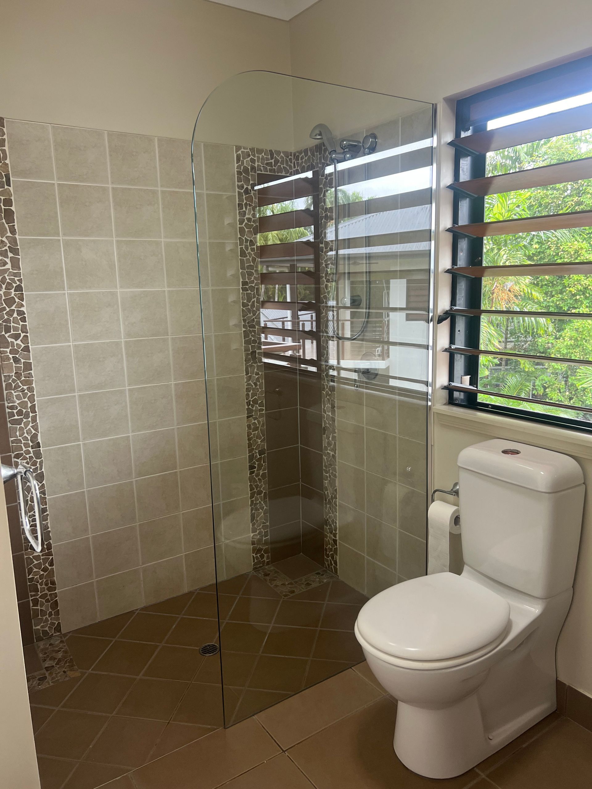 A bathroom with a toilet , shower and window.