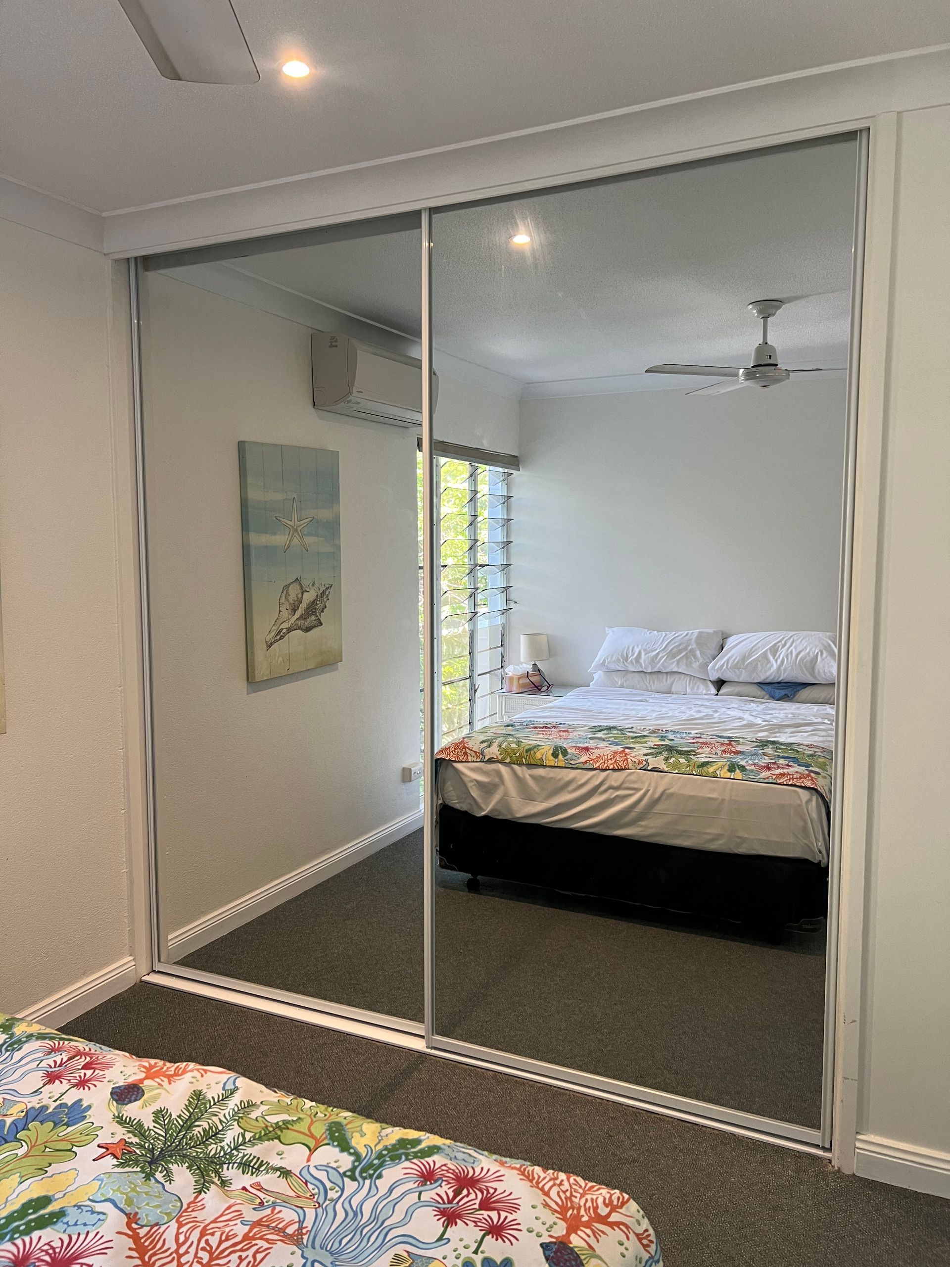 A bedroom with a bed , mirrored sliding doors , and a ceiling fan.