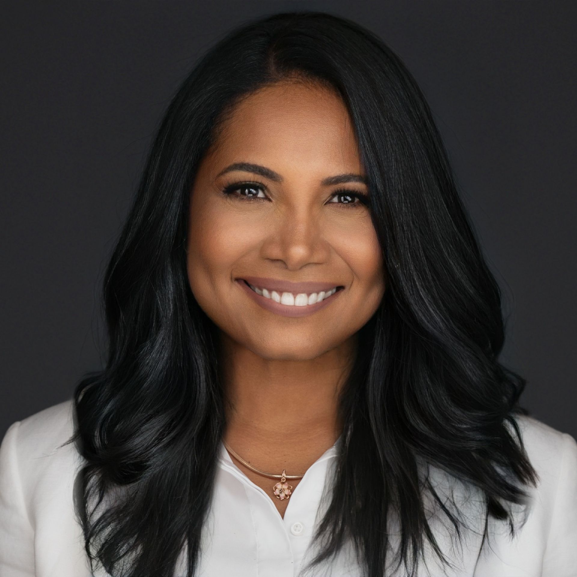 Woman with dark hair, smiling, wearing a light-colored blazer, against a dark backdrop.