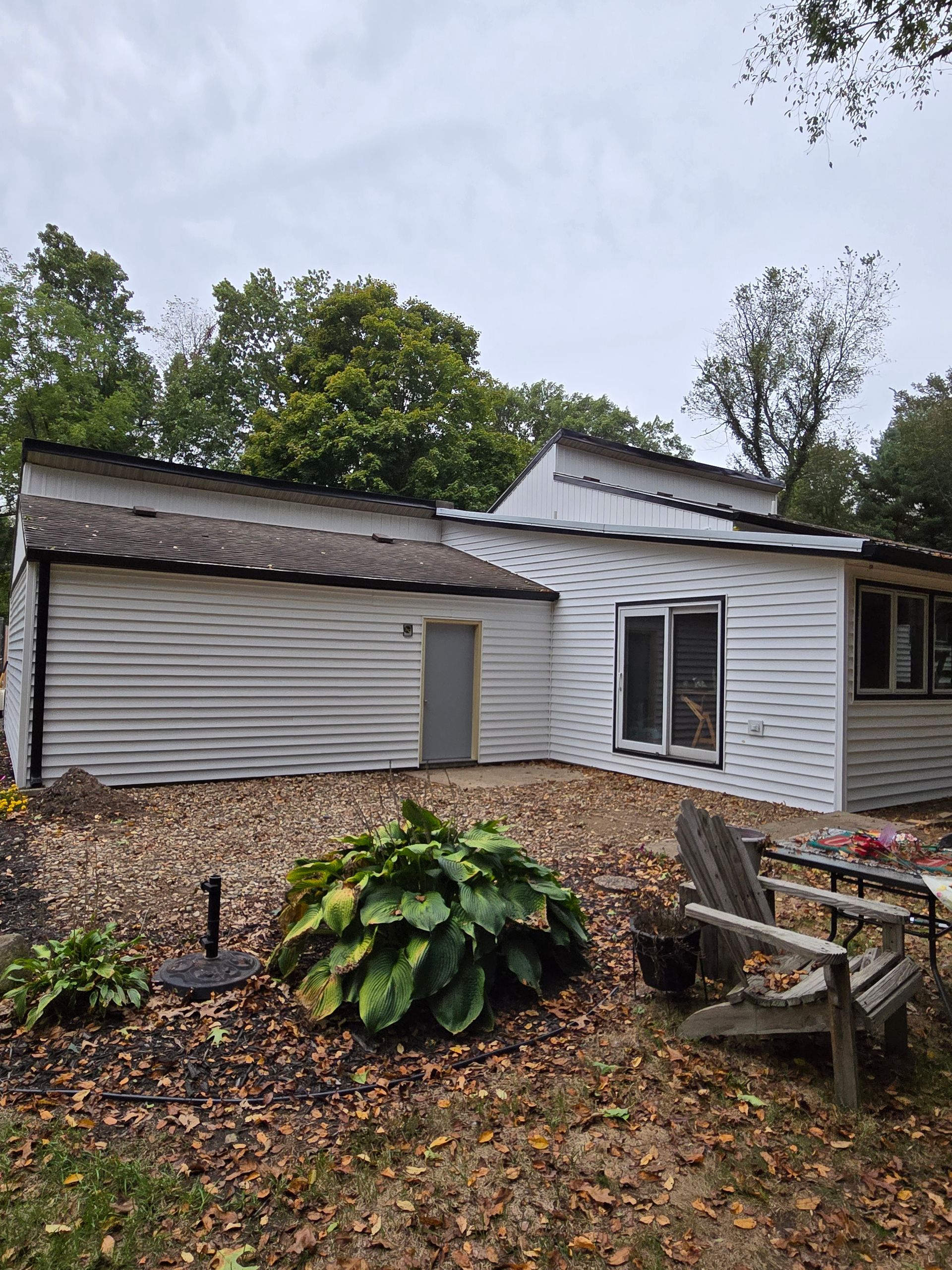 A white house with a lot of leaves on the ground in front of it.