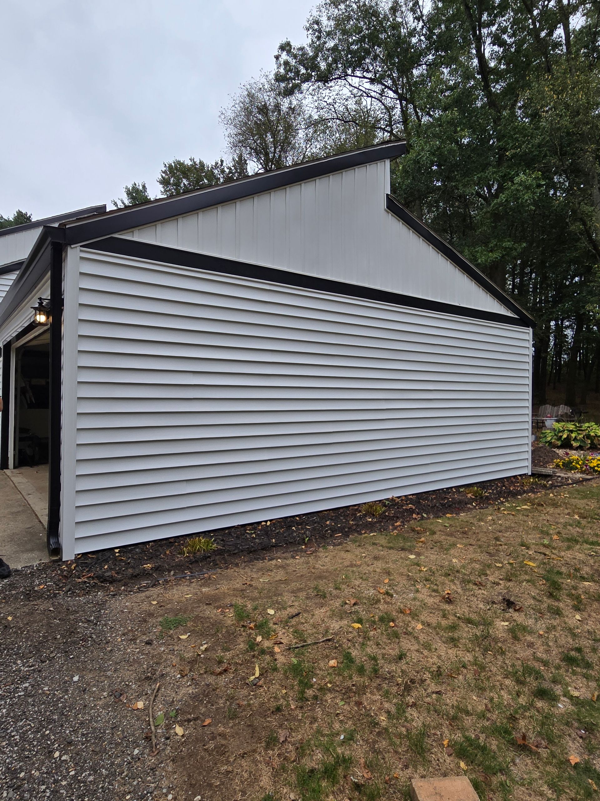 A white garage with a black trim is sitting in the middle of a grassy field.