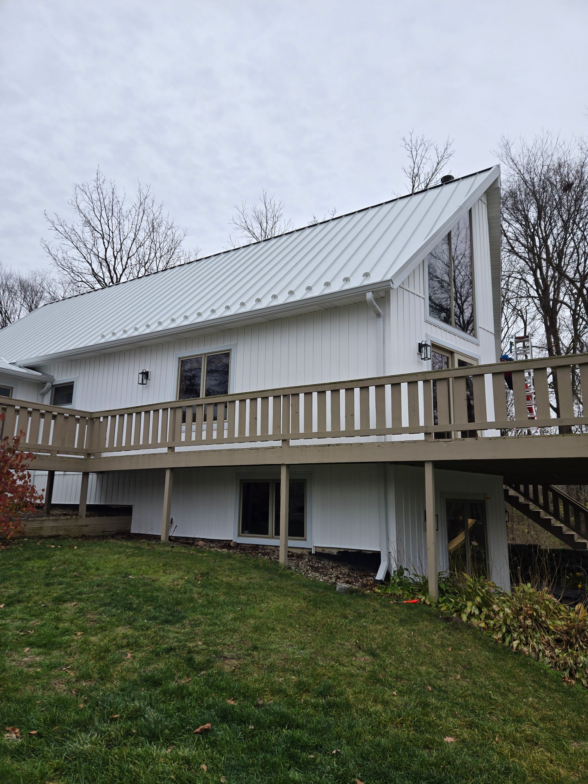 A white house with a metal roof and a wooden deck.