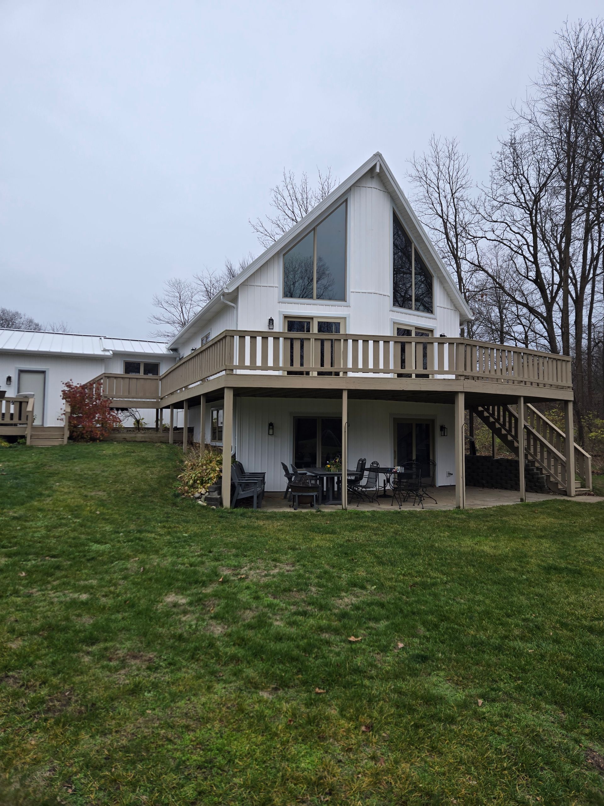A white house with a large deck and a large lawn in front of it.