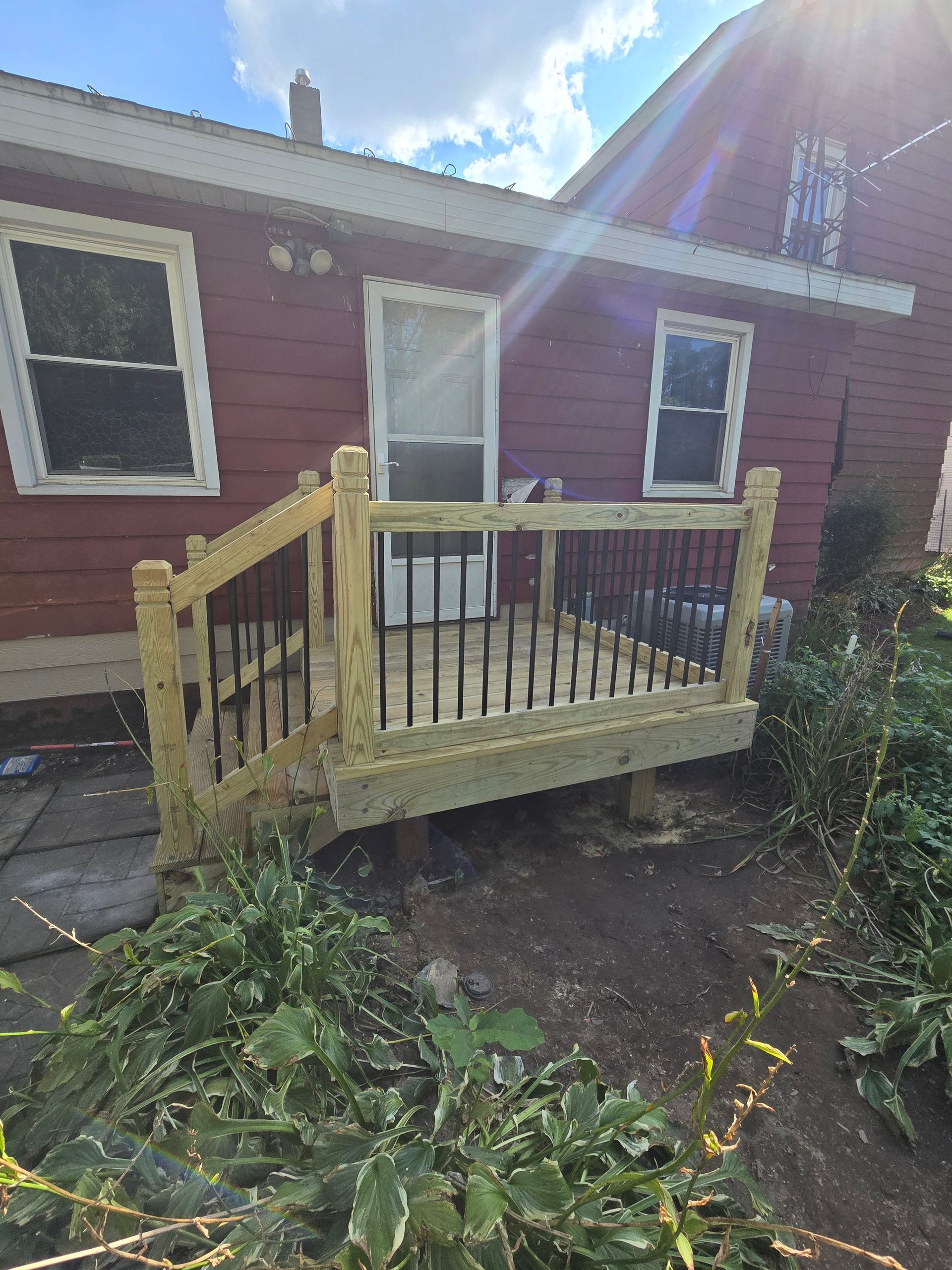 A small wooden deck with black railings and a short staircase is attached to the exterior of a red house.