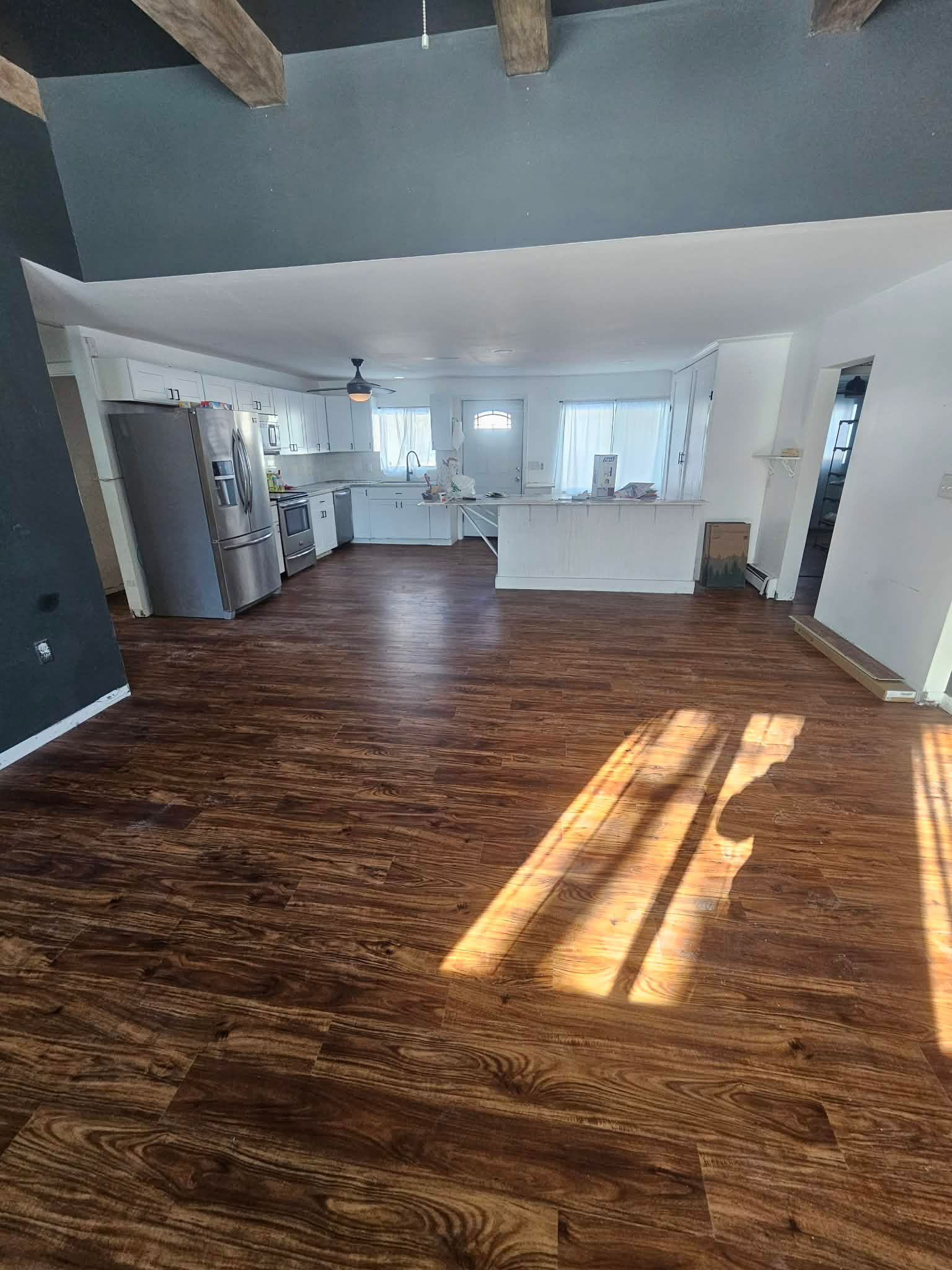 Open-concept kitchen with dark wood flooring, a stainless steel refrigerator, and white cabinets under a dark gray ceiling.