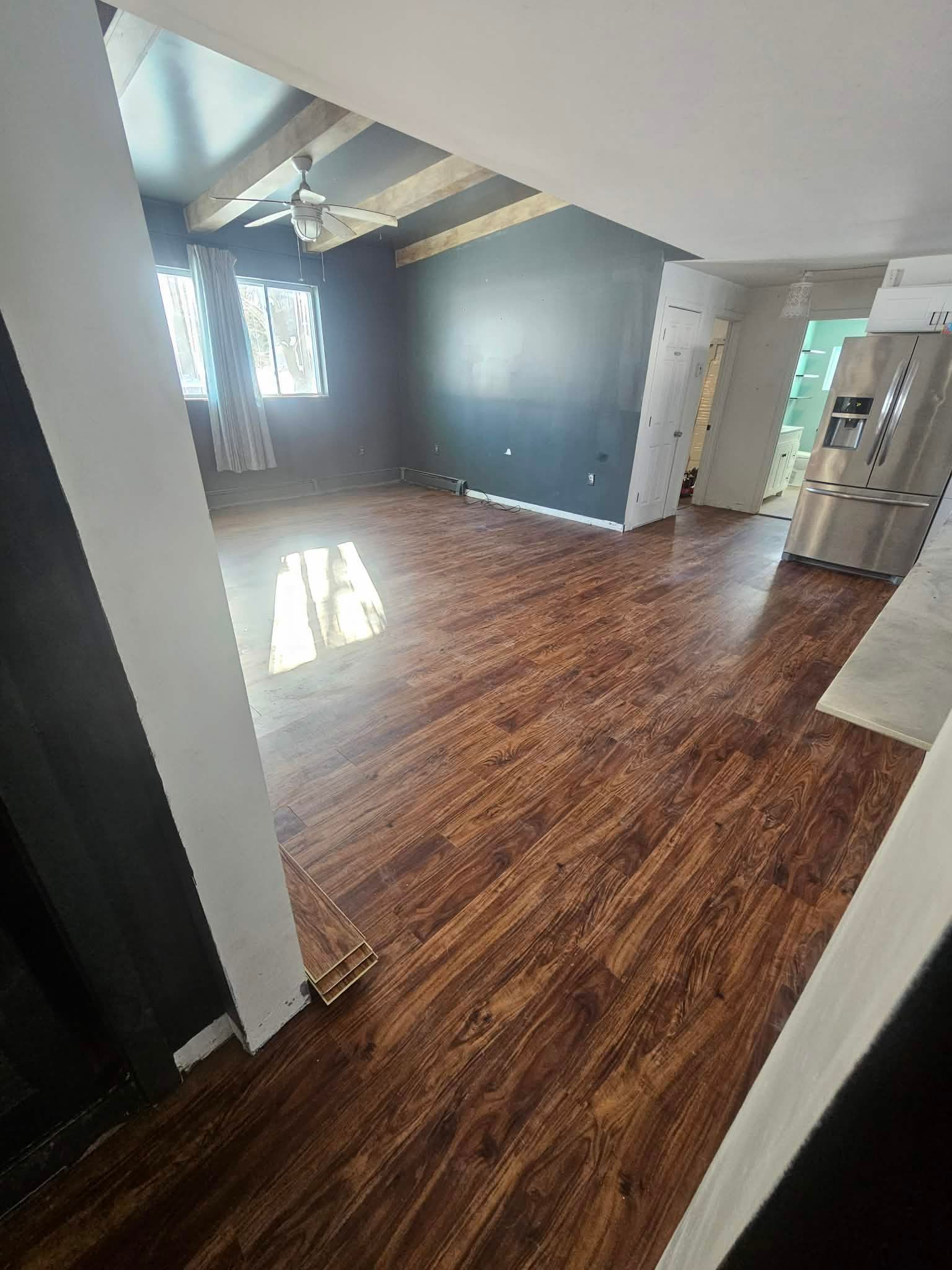An open-concept living area with dark wood-style flooring, white walls, and a charcoal accent wall under vaulted ceilings.