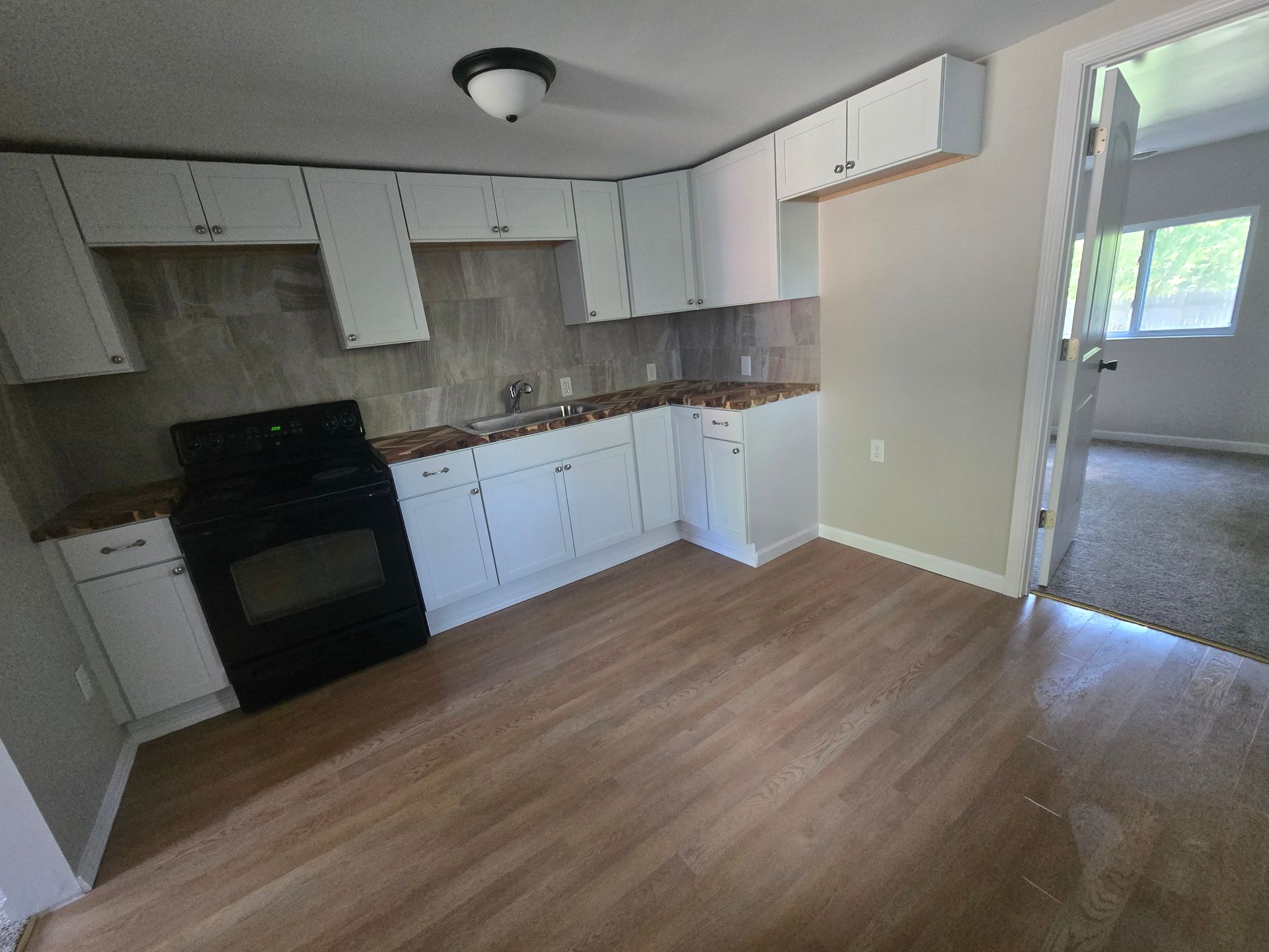 A kitchen with light wood flooring, white cabinets, a black stove, and a beige tiled backsplash.