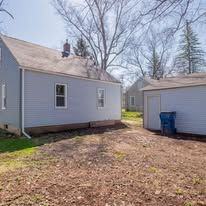 The backyard of a house with a garage and a trash can.