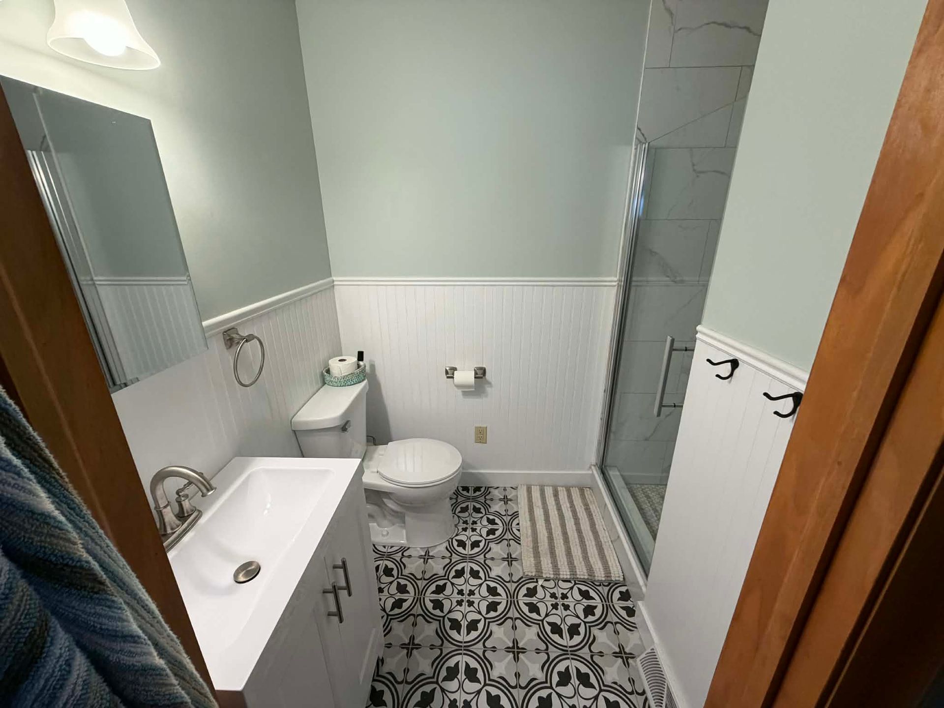 A bright bathroom with patterned tile floors, a white vanity with a sink, a toilet, and a glass-enclosed shower.