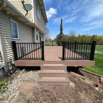 A composite deck with stairs and a black railing is in front of a house.
